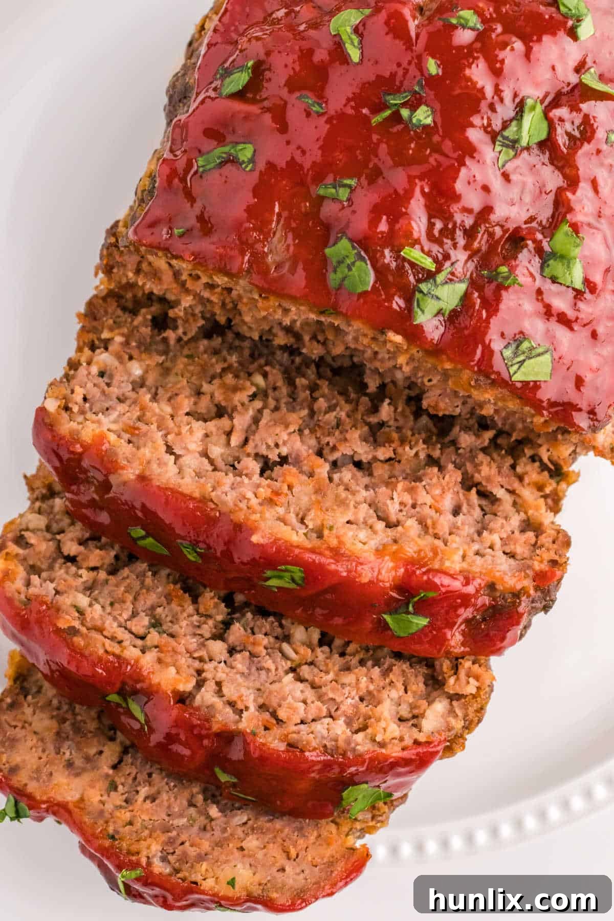 A large meatloaf on a platter, with several slices cut and removed, showcasing its moist interior and delicious glaze.