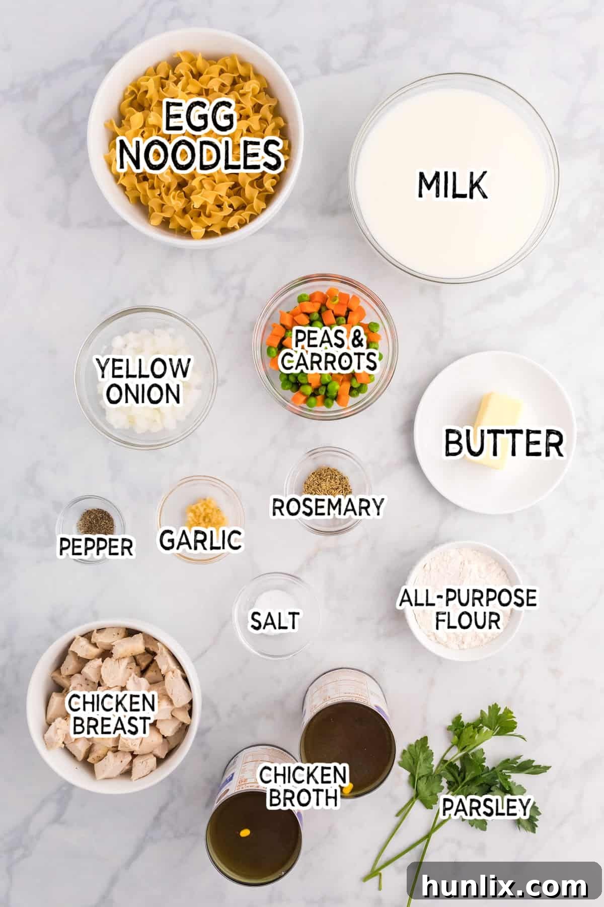 Various fresh and pantry ingredients laid out, including chicken, vegetables, butter, and noodles, ready to make creamy chicken noodle soup.
