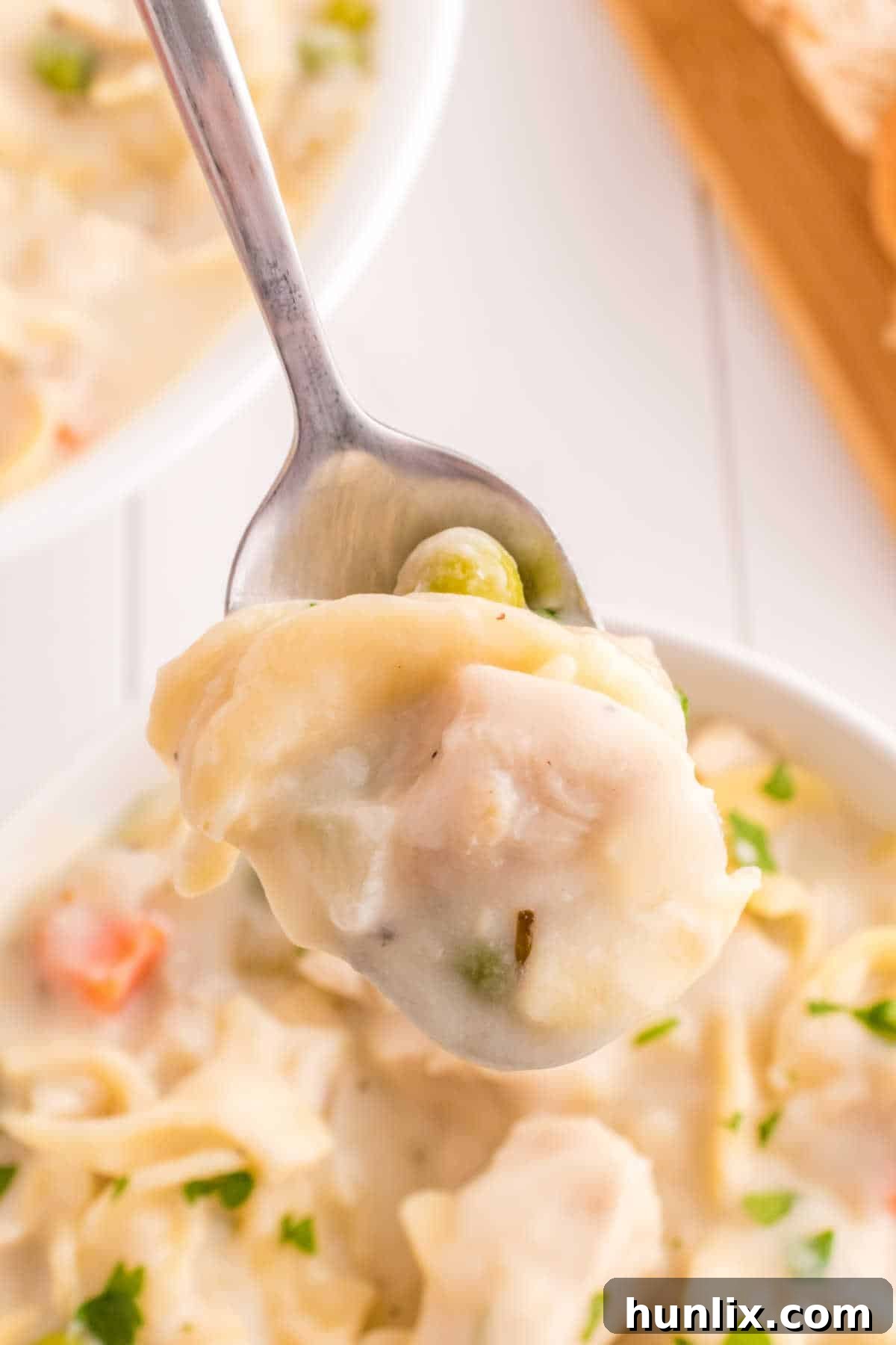 A spoon lifting a perfect bite of creamy chicken noodle soup, showing the noodles, chicken, and rich broth.