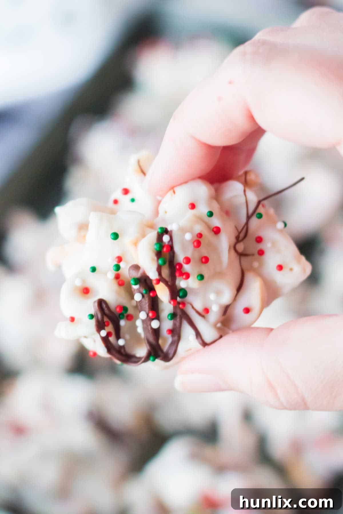 A hand delicately holding a single peppermint crockpot candy cluster, showcasing its texture and festive appeal.