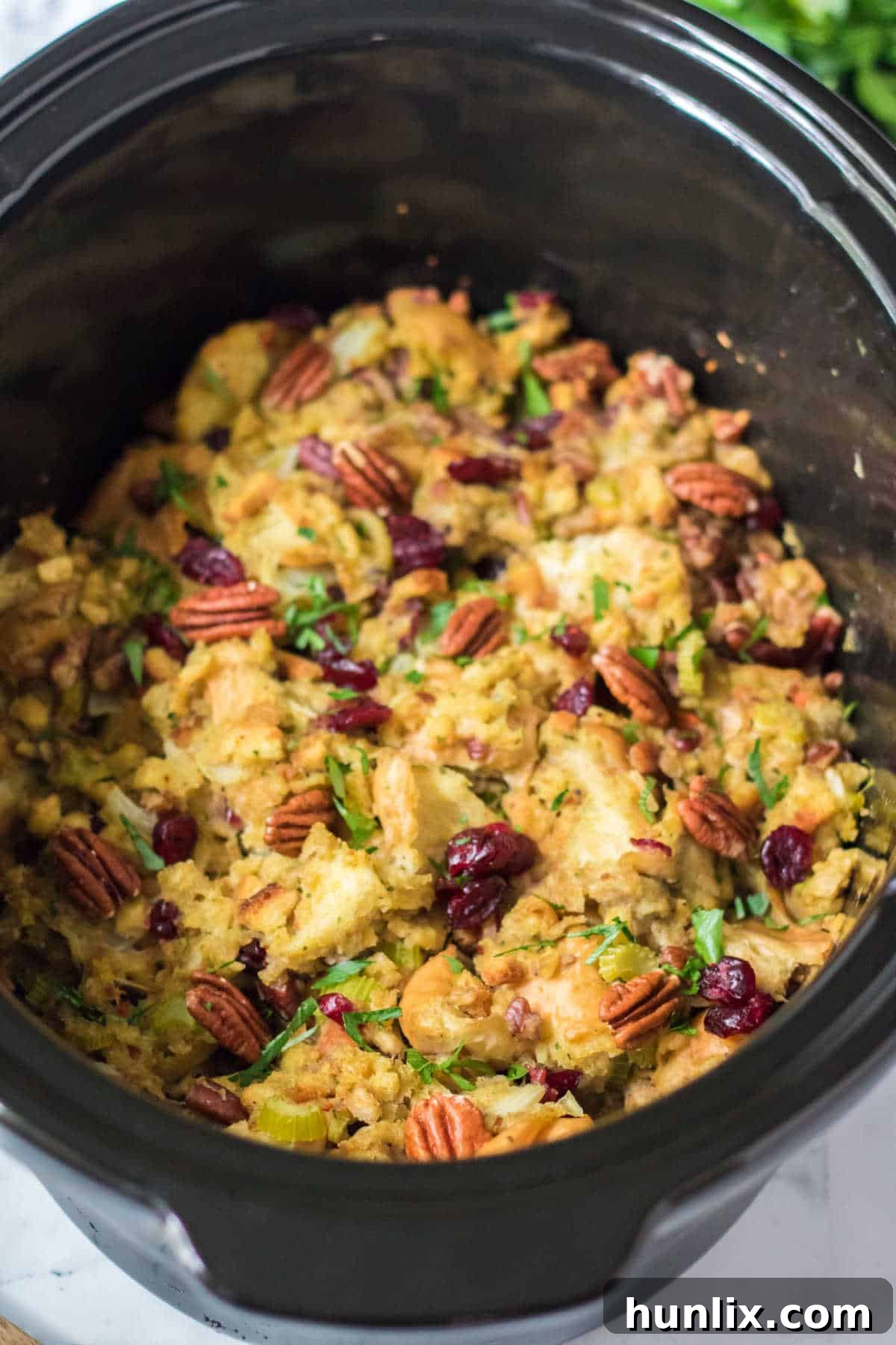 Effortless Slow Cooker Cranberry Pecan Stuffing 2 Cranberry pecan stuffing in a black crockpot, garnished and ready to be served at a holiday meal.