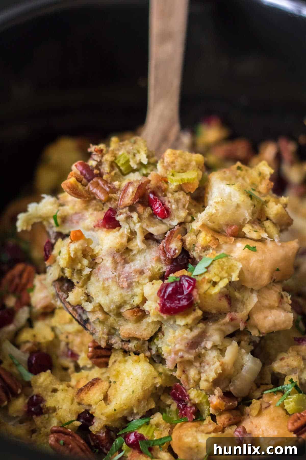 Effortless Slow Cooker Cranberry Pecan Stuffing 6 Cranberry pecan stuffing served directly from a black crockpot with a wooden serving spoon, highlighting its festive appeal and ease of serving.