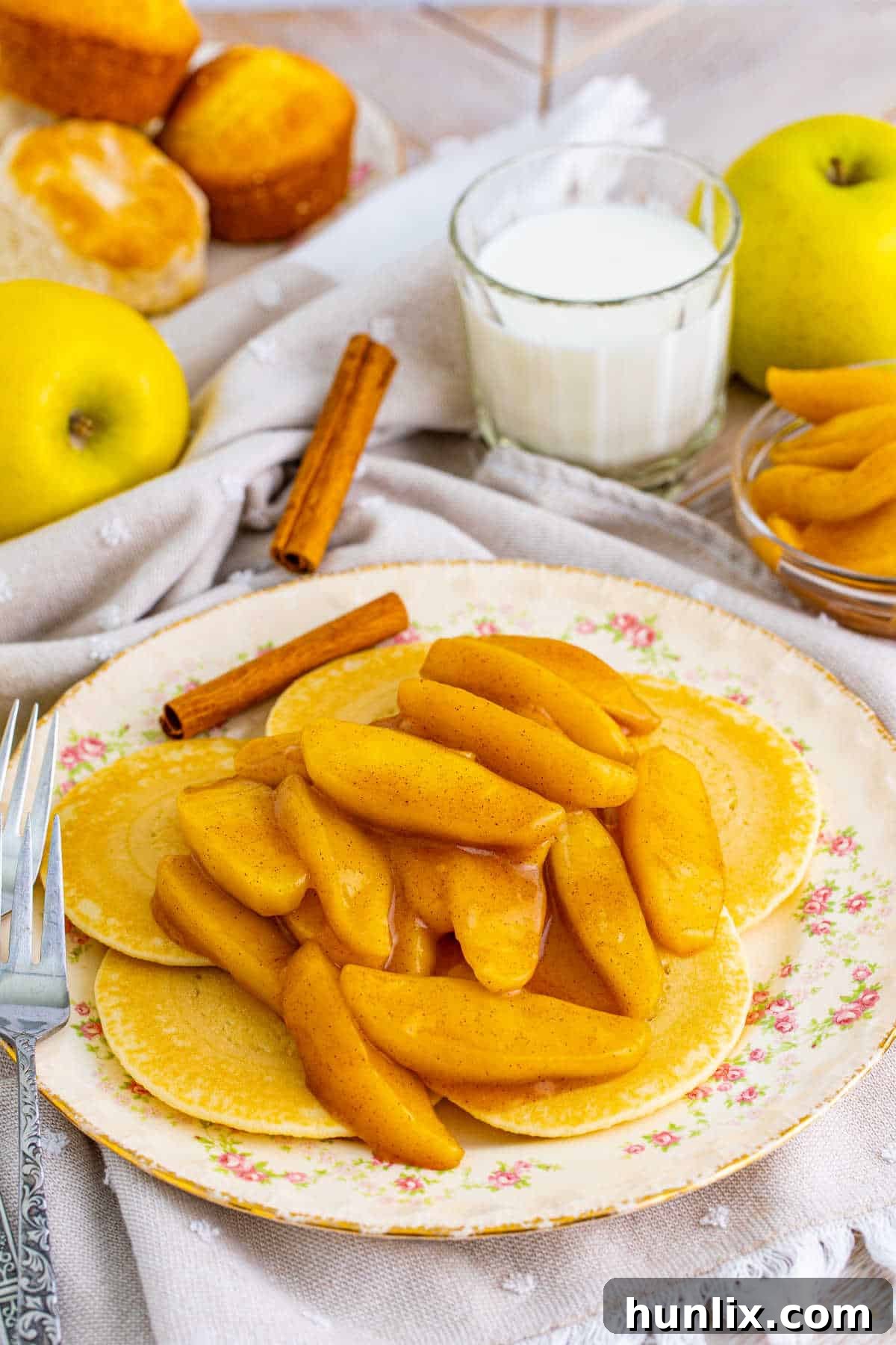 Golden-brown pancakes topped with a generous serving of Cracker Barrel Fried Apples, drizzled with syrup, and ready to be served on a white plate, highlighting a perfect breakfast or brunch dish.