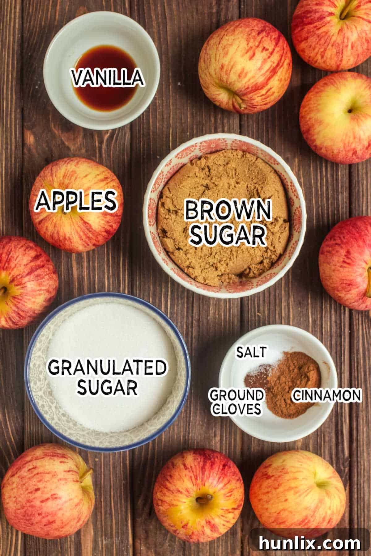A curated display of ingredients for Instant Pot apple butter, including a bowl of chopped apples, brown sugar, granulated sugar, cinnamon, ground cloves, salt, and vanilla extract.