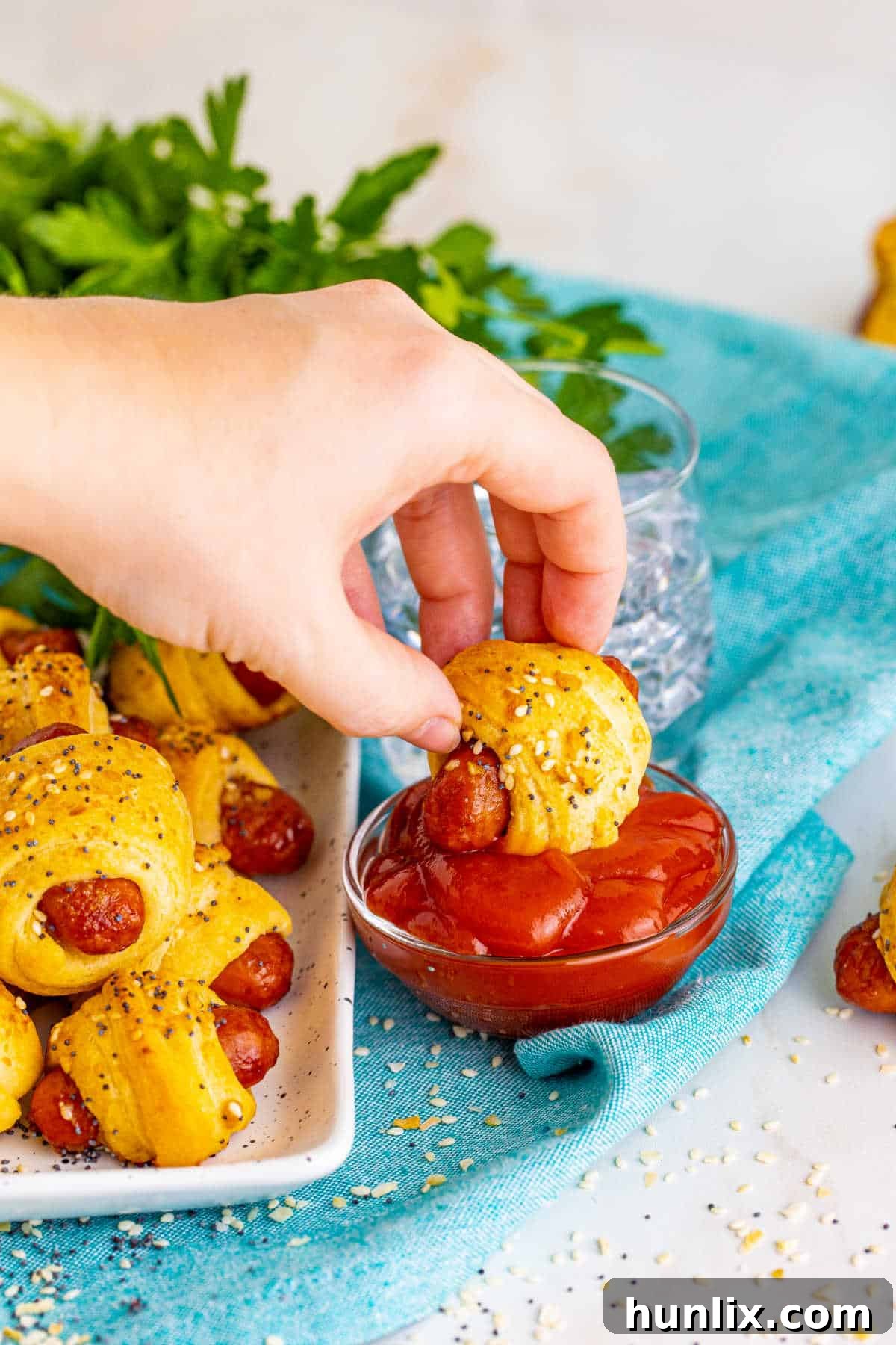 Snuggle Sausages 7 A hand dipping a pig in a blanket into ketchup.