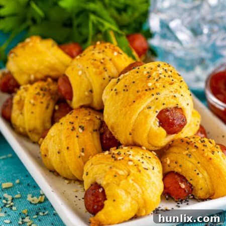 Close-up of baked Pigs in a Blanket on a platter, garnished with parsley.