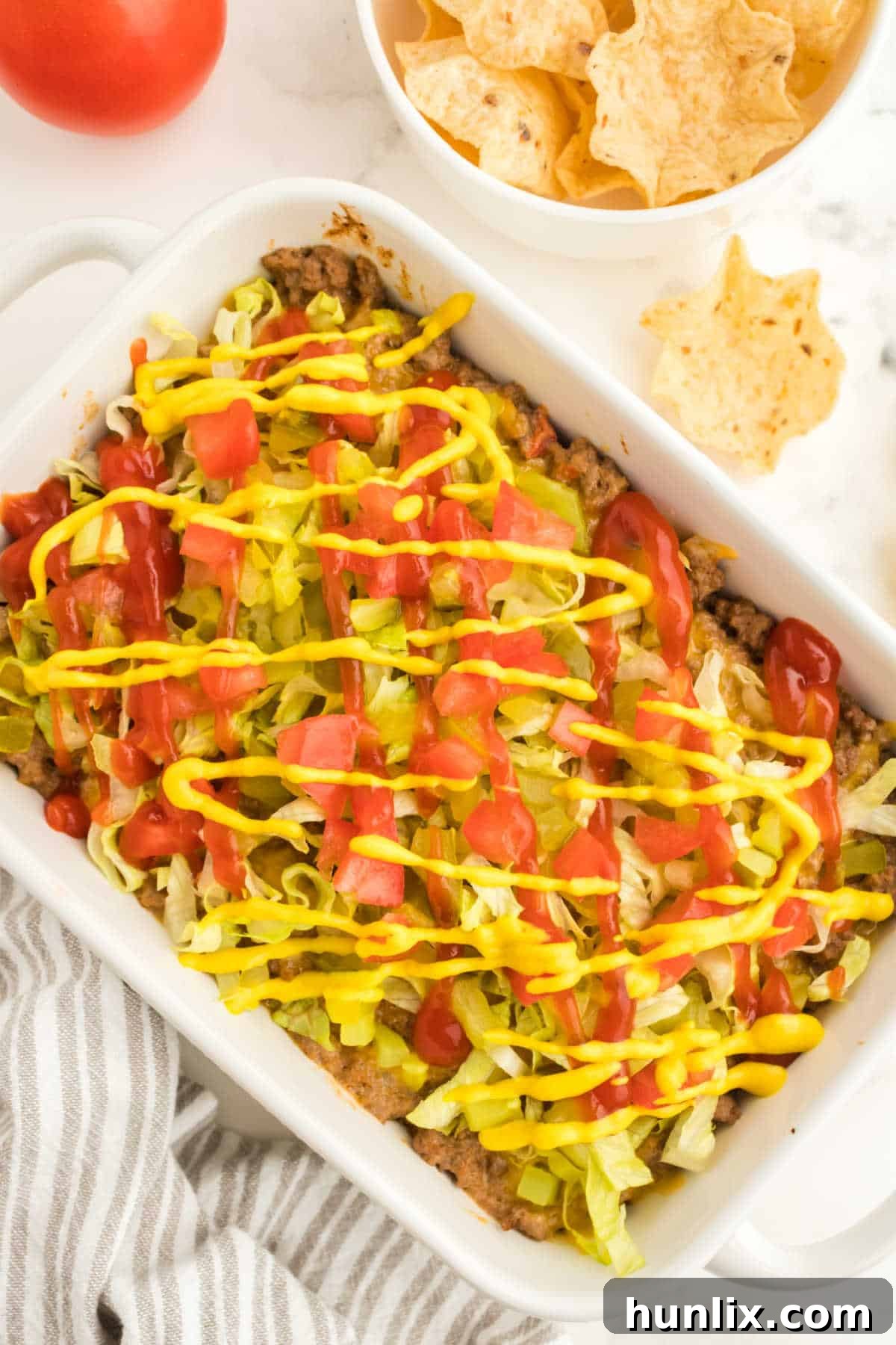 A baking dish with bubbling cheeseburger dip, garnished with fresh toppings, ready to be served at a party.