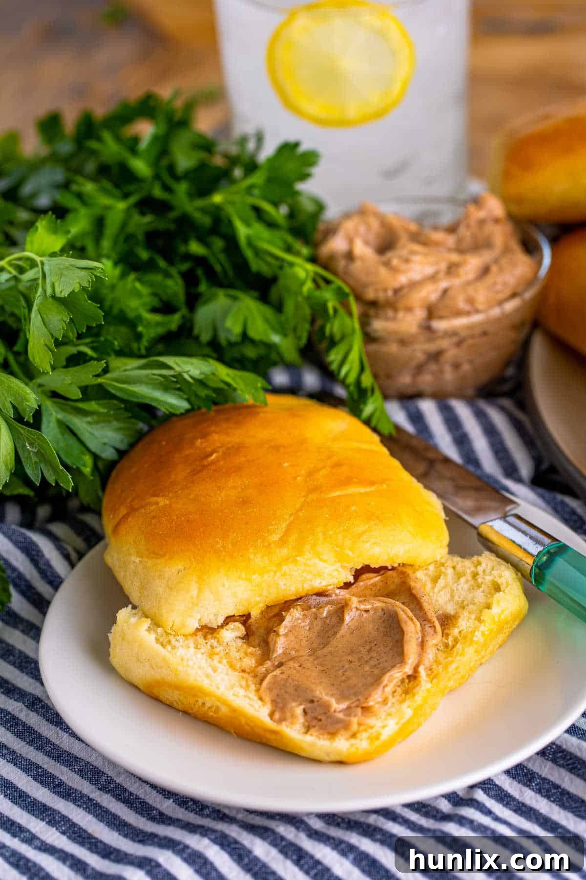 A perfect Copycat Texas Roadhouse Roll, sliced in half and generously spread with cinnamon butter, on a simple white plate.