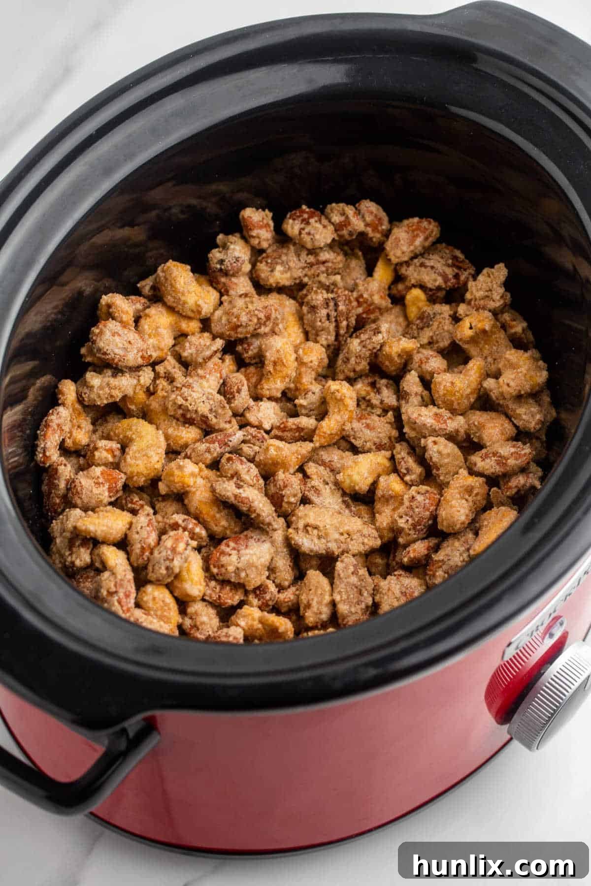 Crockpot filled with cinnamon sugar coated mixed nuts, ready for slow cooking.