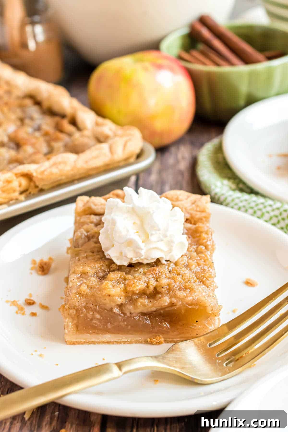 Sheet Pan Apple Pie 12 A beautiful slice of apple slab pie topped with a generous dollop of whipped cream on a plate with a fork.