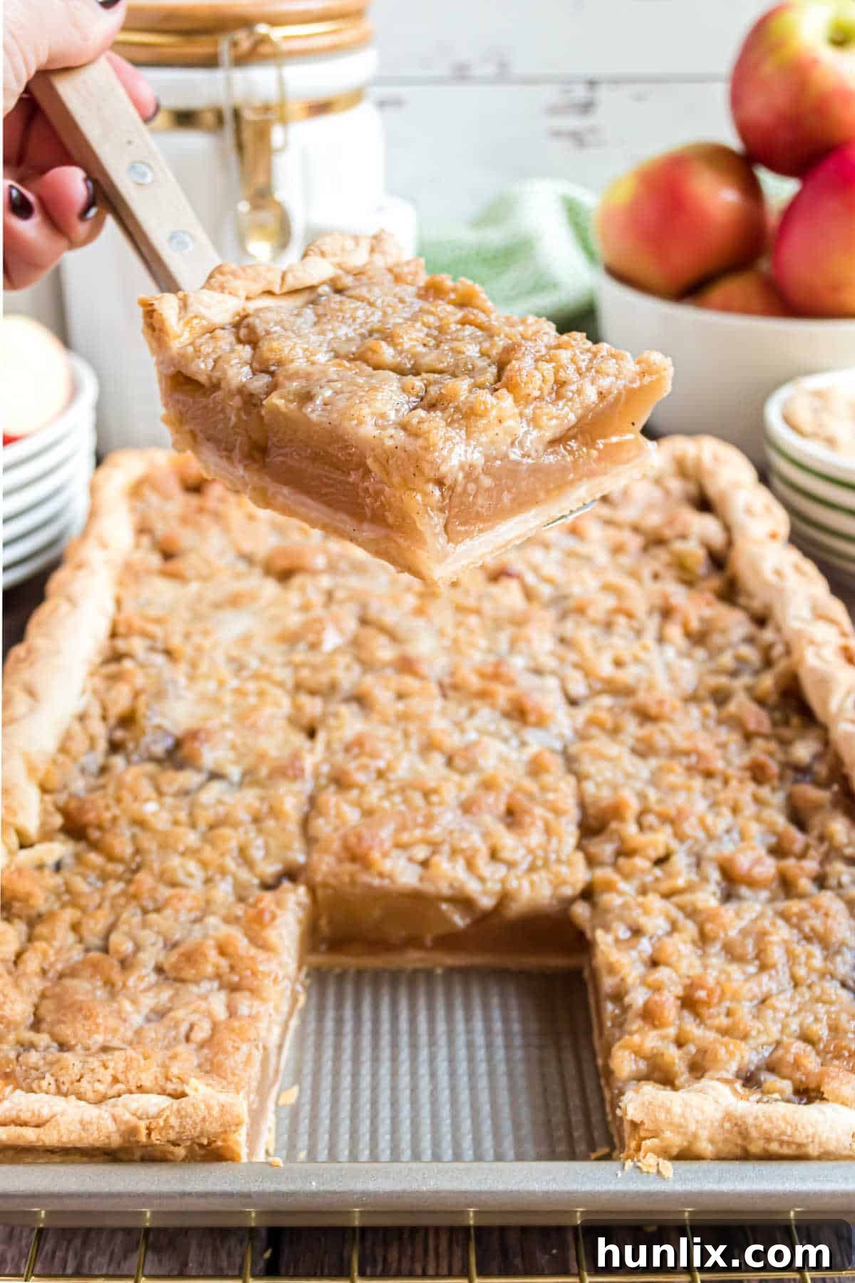 Sheet Pan Apple Pie 9 A serving spatula lifting a perfect square slice of apple slab pie, showcasing its layers of crust, apple filling, and crumb topping.