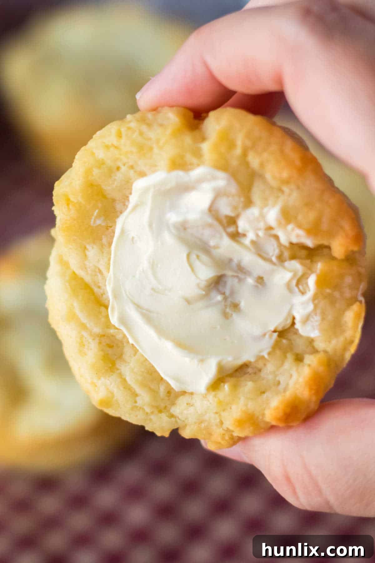 A hand holding a perfectly buttered sour cream biscuit, highlighting its soft, inviting texture.