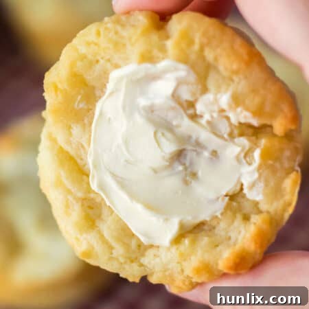 A hand holding a buttered biscuit.