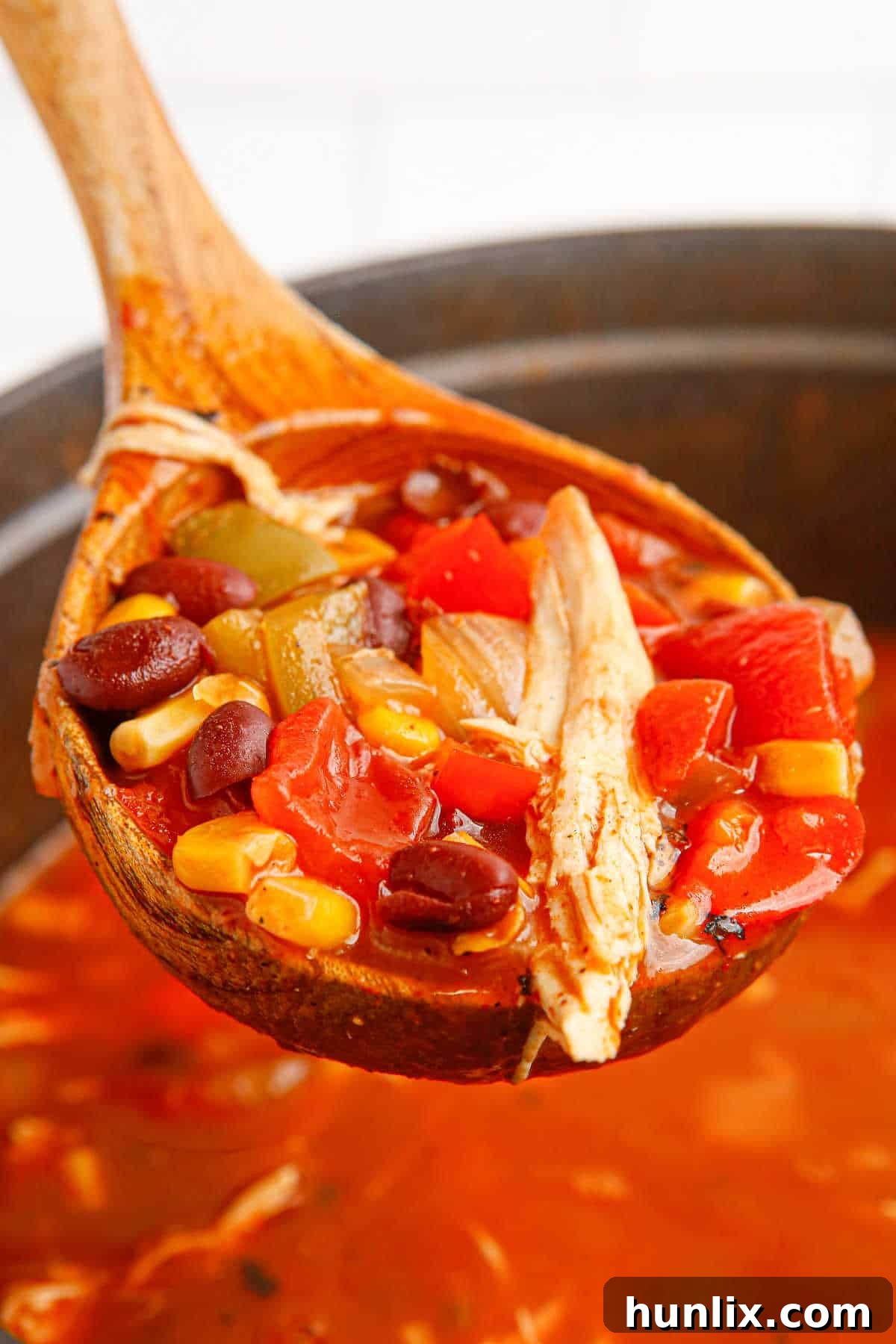 A ladle full of vibrant Chicken Fajita Soup, garnished with fresh cilantro and cheese, being served from a large pot.