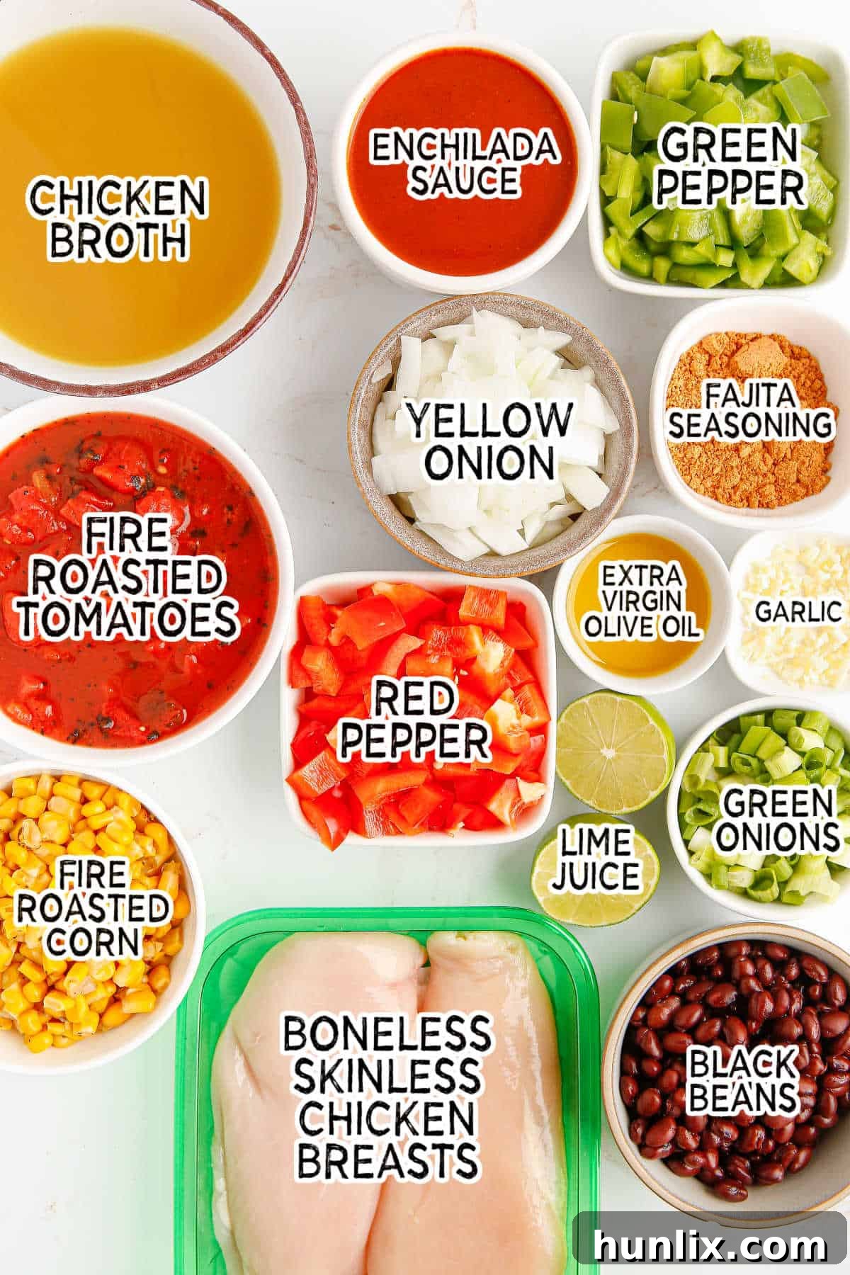 A flat lay of fresh ingredients for chicken fajita soup including chicken breasts, bell peppers, onions, garlic, canned goods, and spices, arranged neatly on a wooden surface.