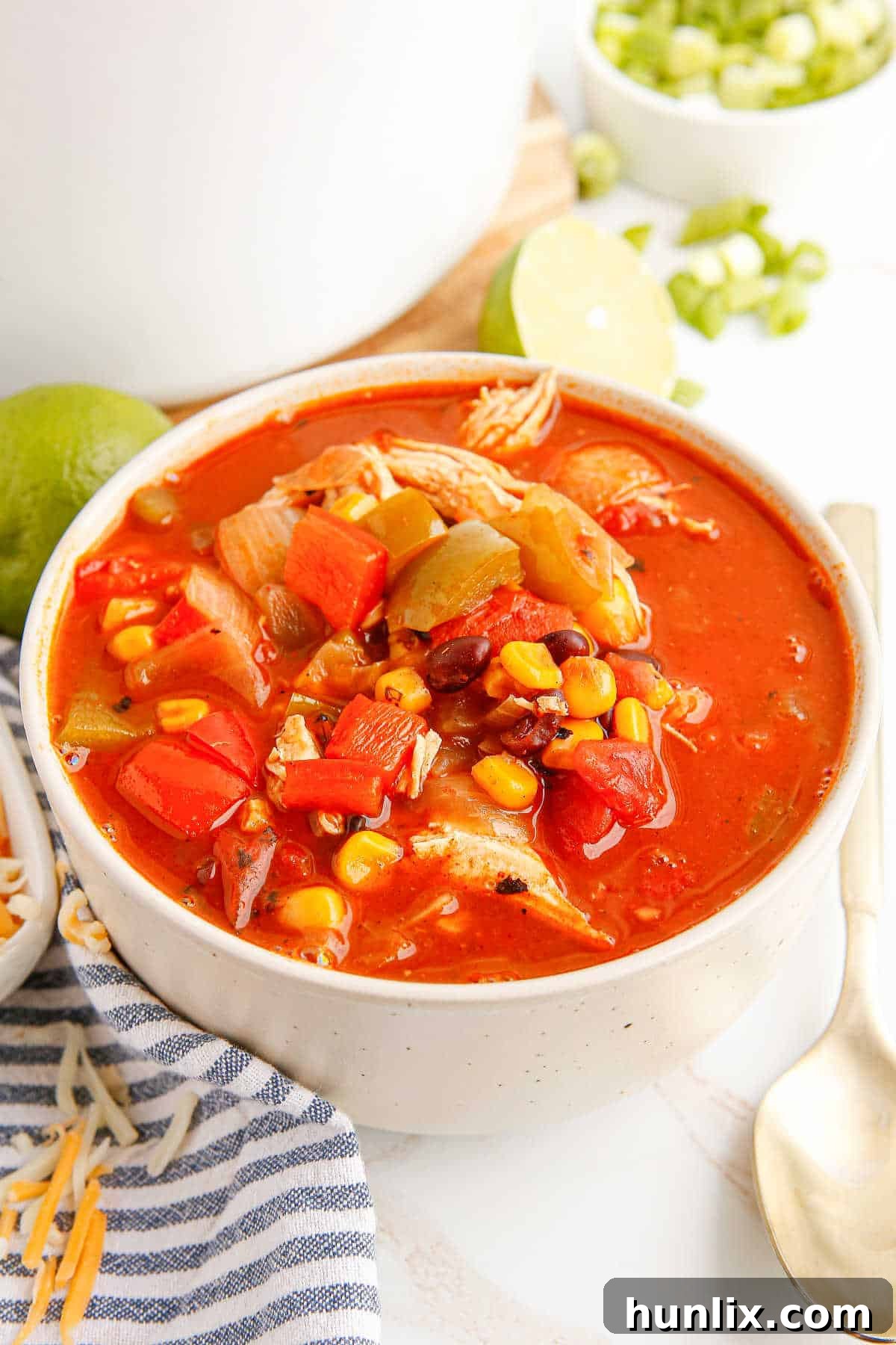 A vibrant bowl of chicken fajita soup with a spoon, garnished with green onions and shredded cheese on a wooden table.