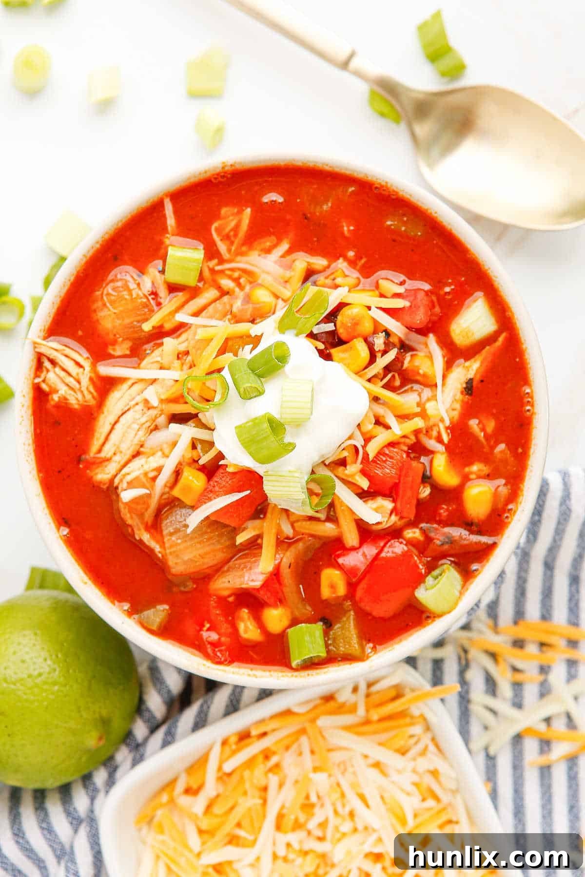 Close-up of a bowl of chicken fajita soup with a spoon, highlighting the texture and vibrant colors of the ingredients, on a wooden background.
