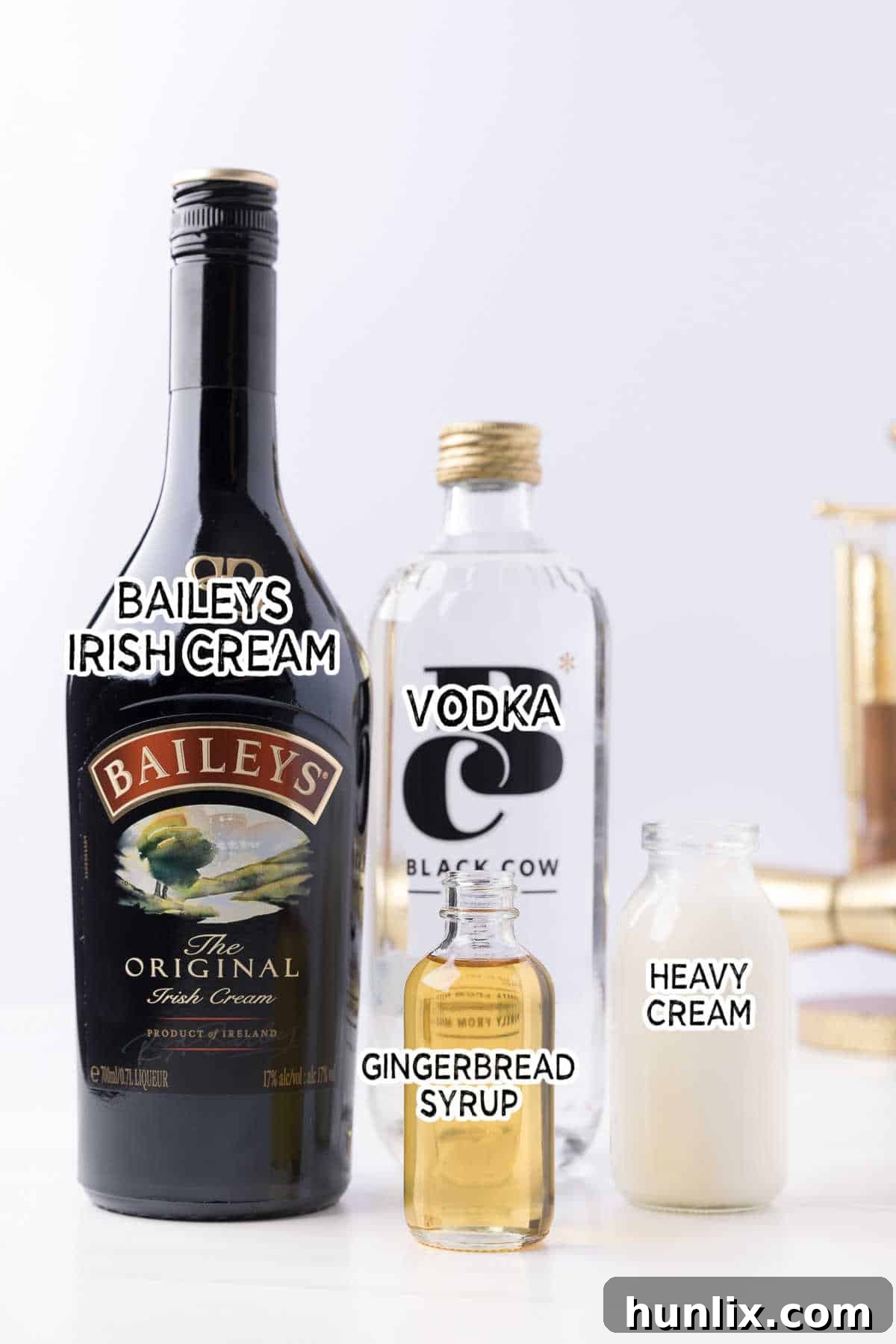 All ingredients laid out on a table to make a gingerbread martini, including bottles of Bailey's, vodka, heavy cream, and gingerbread syrup.