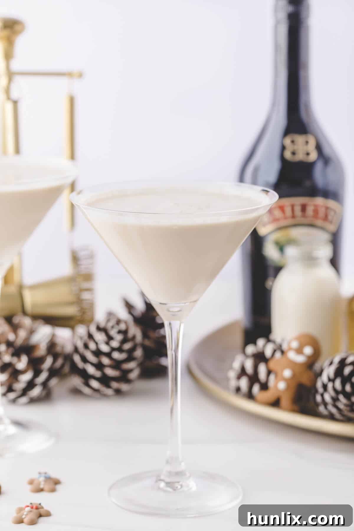 A gingerbread martini with a cinnamon stick garnish, surrounded by festive holiday decor like pinecones and Christmas lights.