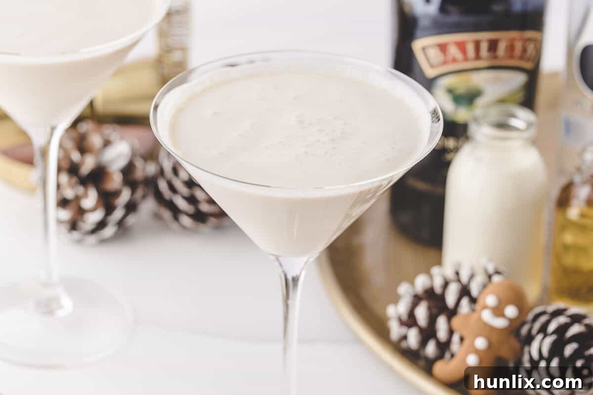 A gingerbread martini decorated with a cinnamon stick and a small gingerbread cookie, placed among holiday decorations.