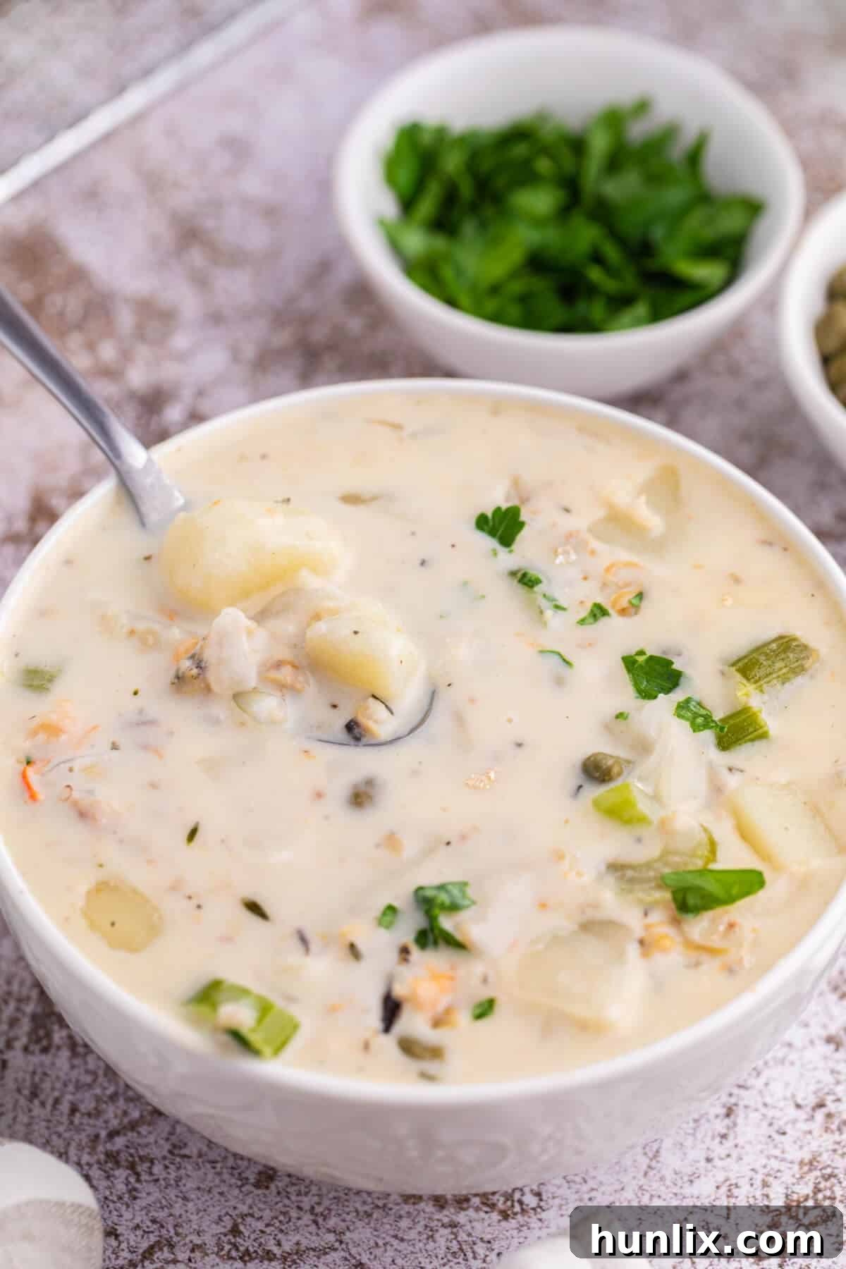 Coastal Comfort Chowder 6 A comforting white bowl of seafood chowder, served with a spoon, highlighting the creamy texture and hearty ingredients within.