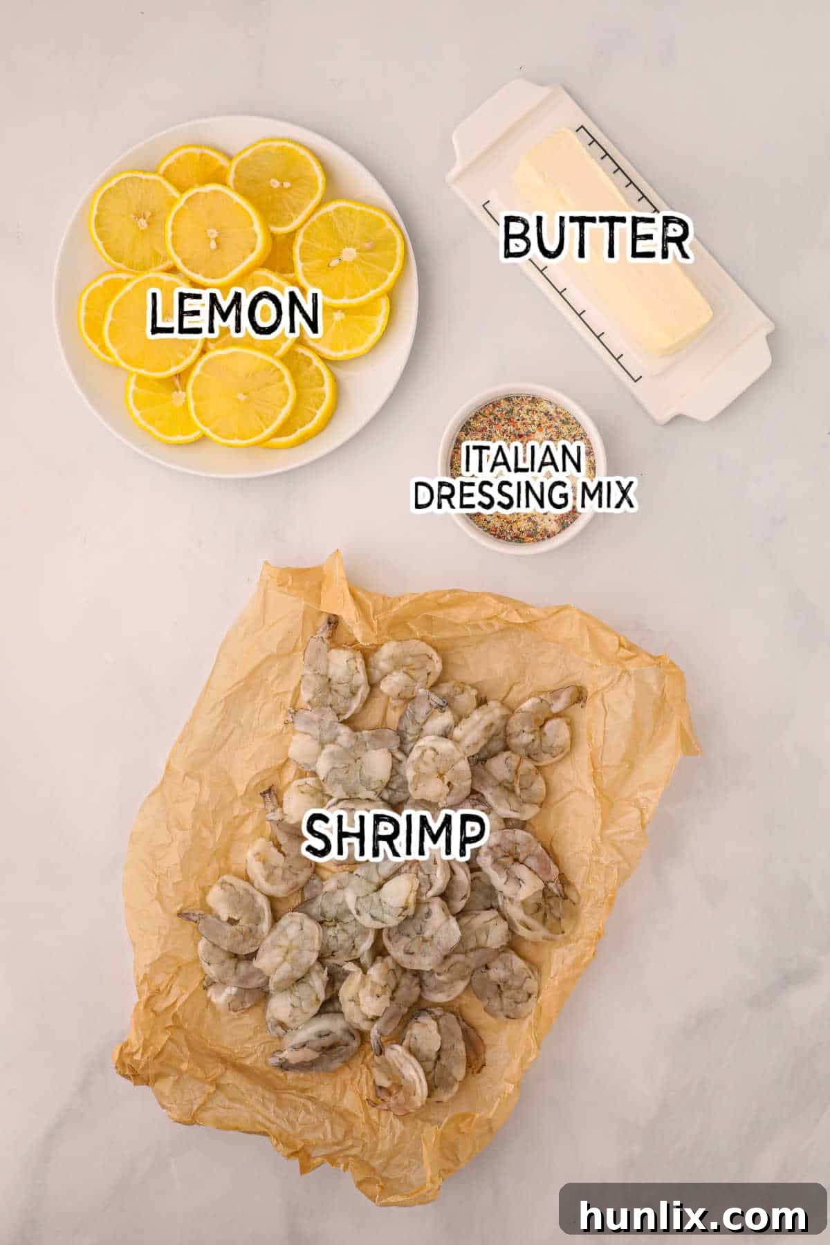 Crispy Air Fryer Shrimp 3 Ingredients for air fryer shrimp laid out on a white background, including butter, lemon, Italian seasoning, and fresh shrimp.