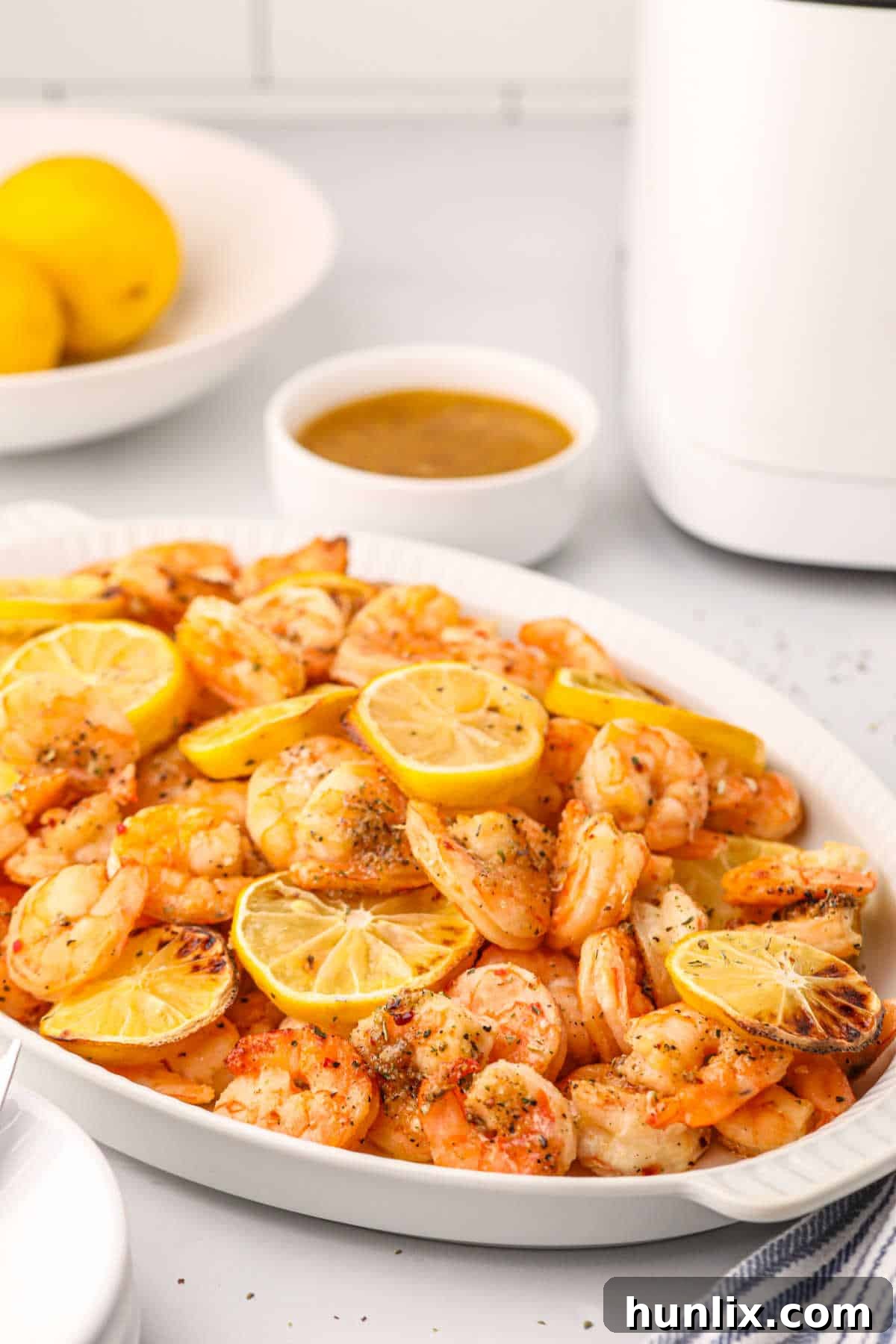 Crispy Air Fryer Shrimp 6 Delicious seasoned air fryer shrimp arranged neatly on a white platter, garnished with lemon wedges.
