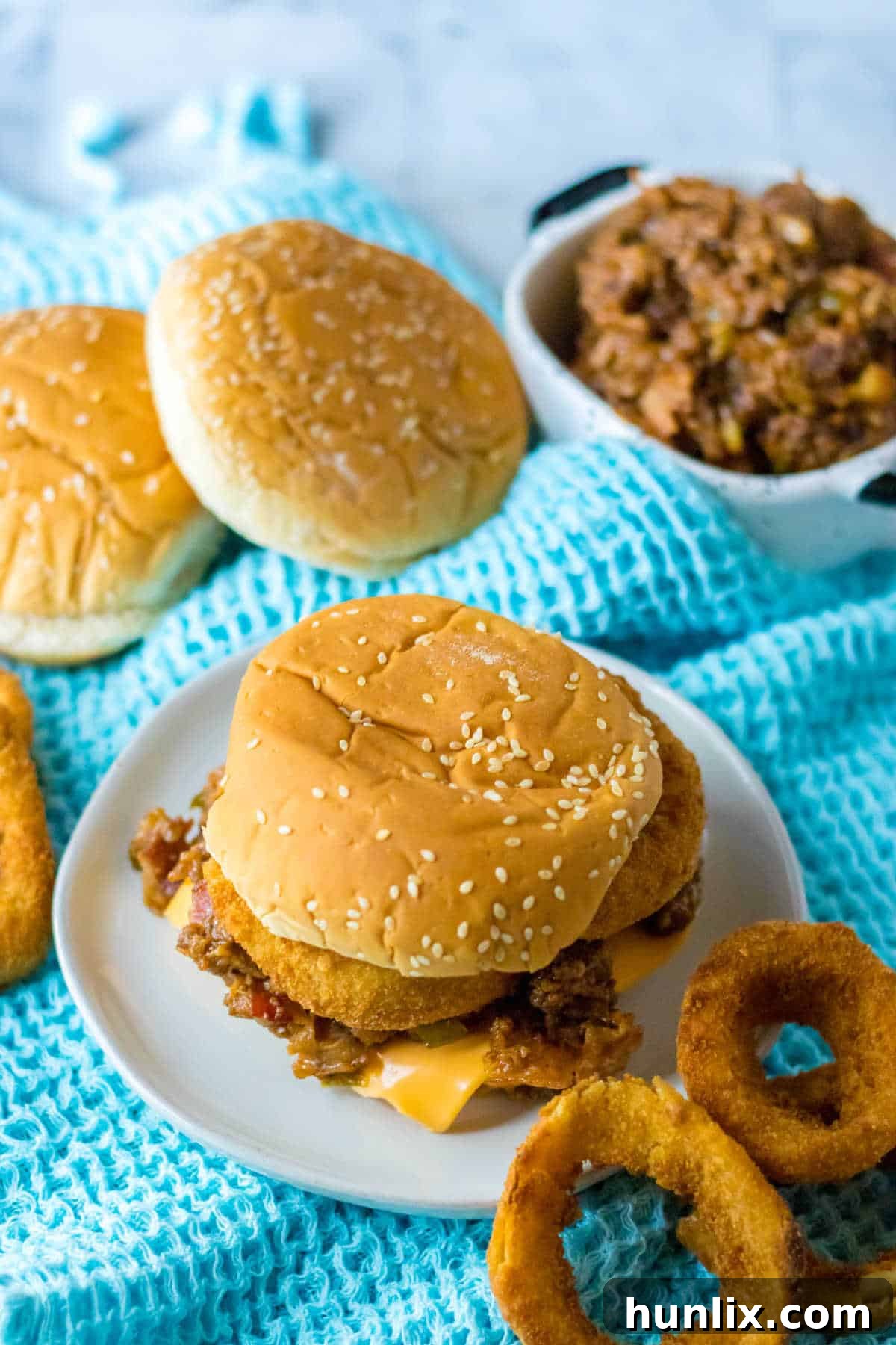 A perfectly assembled rodeo sloppy joe on a plate, with golden onion rings on top.