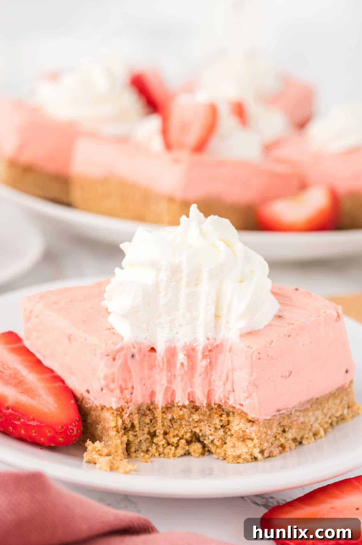A single Strawberry Cheesecake Bar on a plate with a bite taken out, showing the creamy filling and crust layers.