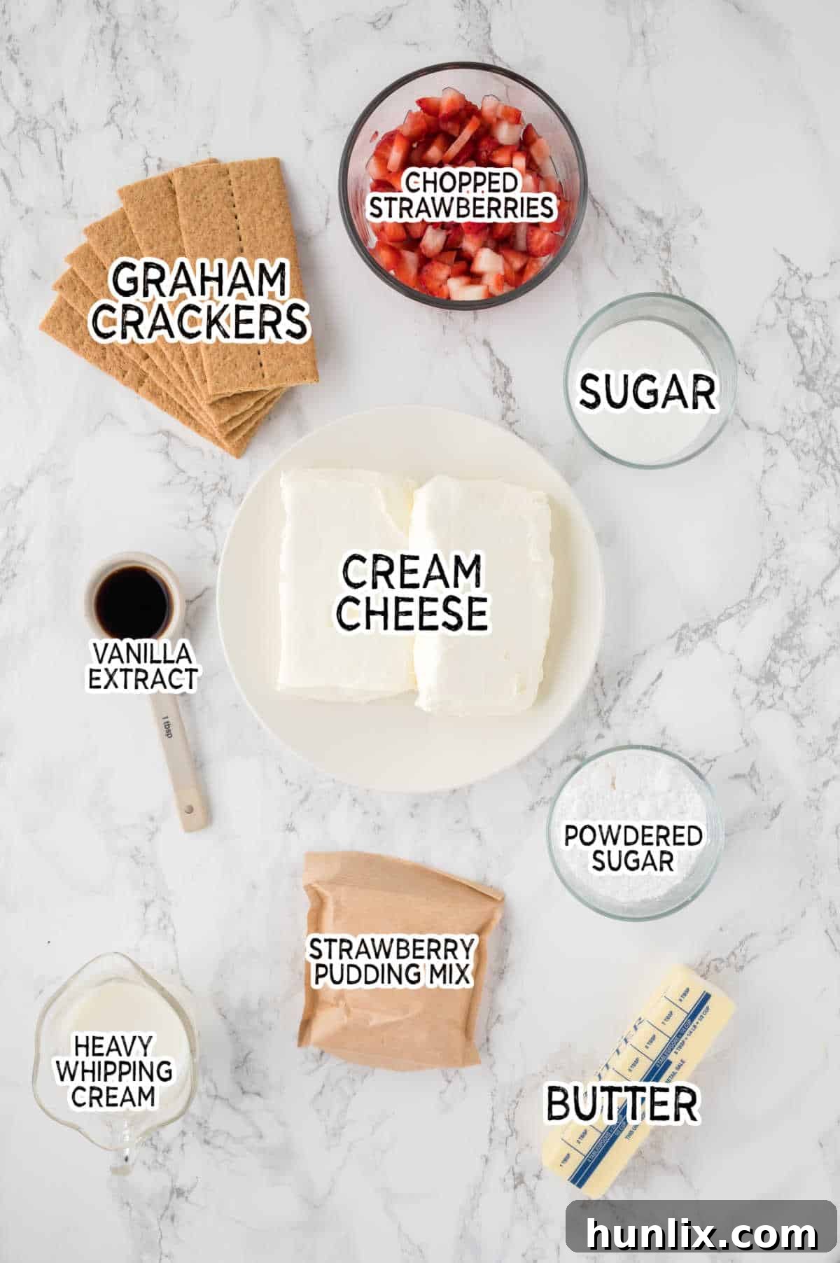 A beautiful array of fresh ingredients for strawberry cheesecake bars laid out on a white marble counter, including graham crackers, cream cheese, strawberries, and butter.
