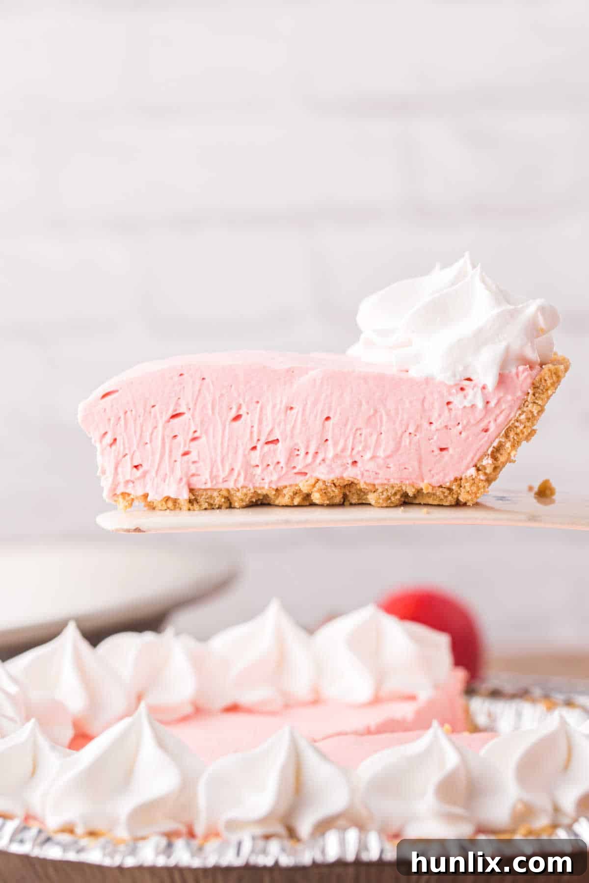 Neon Nectar Pie 2 A spatula lifting up a perfect slice of bright pink Kool-Aid pie, revealing its creamy texture and graham cracker crust.
