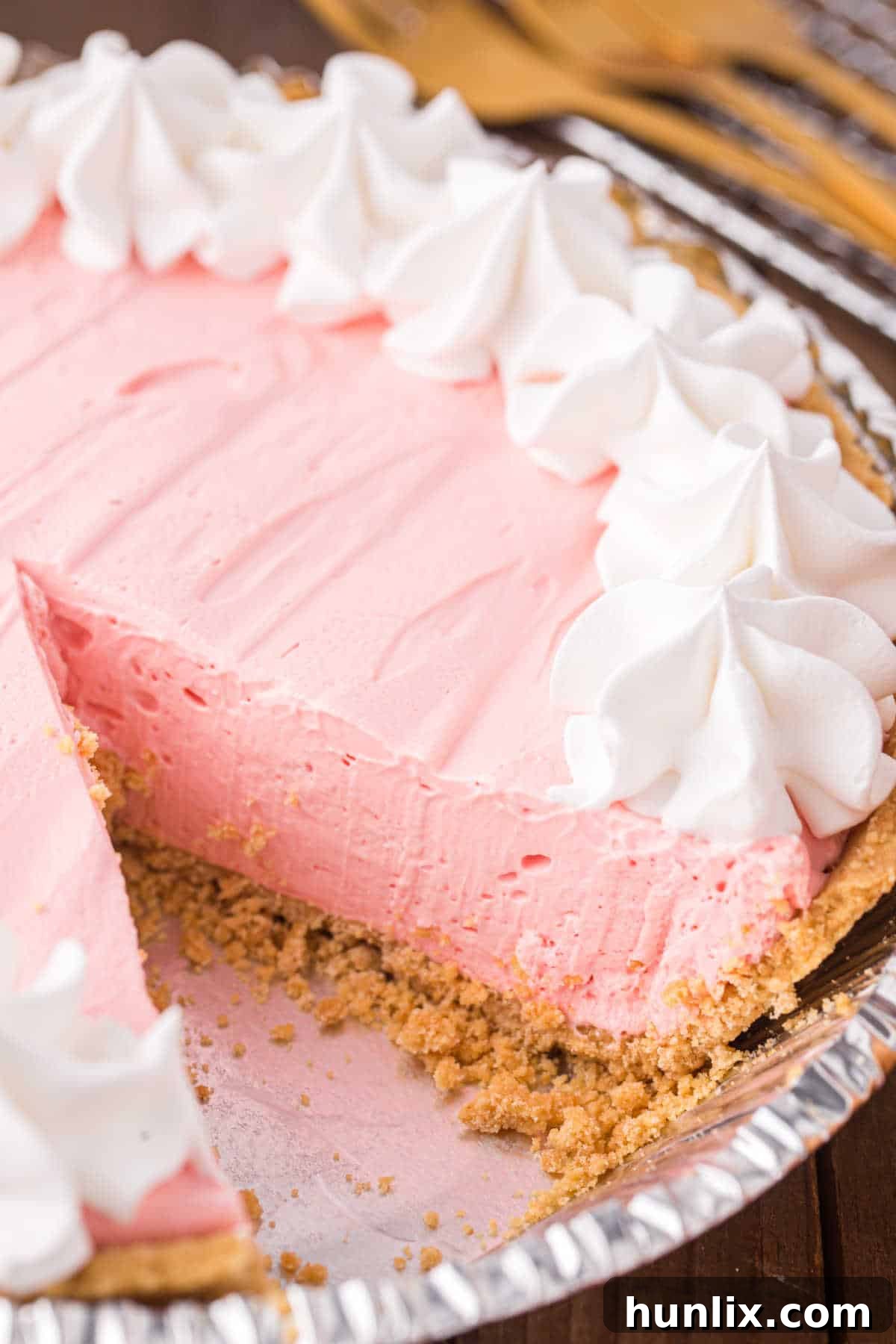Neon Nectar Pie 7 A whole Kool-Aid pie with a slice carefully removed, showcasing its creamy interior and vibrant pink color, garnished with whipped cream and a strawberry slice.