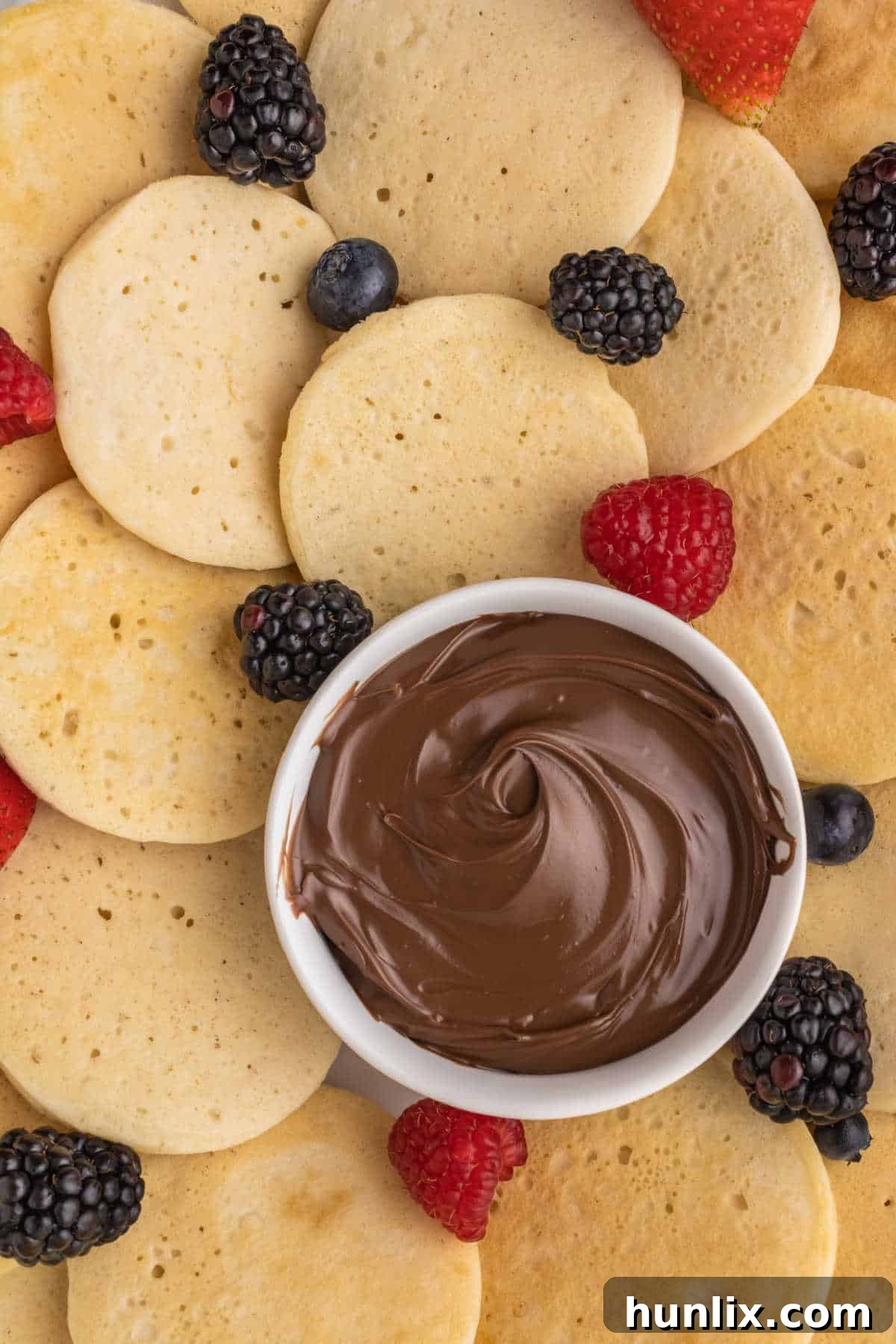 A platter of mini pancakes with a bowl of Nutella.