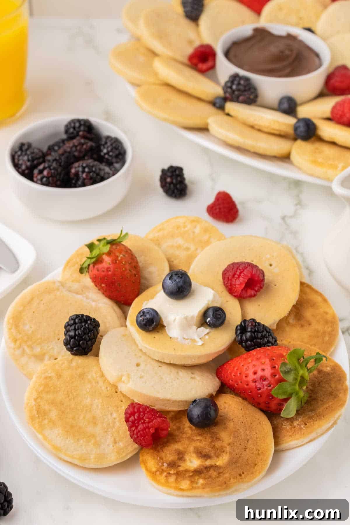 A plate of mini pancakes with butter and fresh berries.