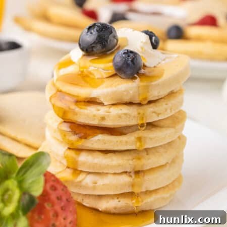 A stack of mini pancakes topped with butter, blueberries and maple syrup.
