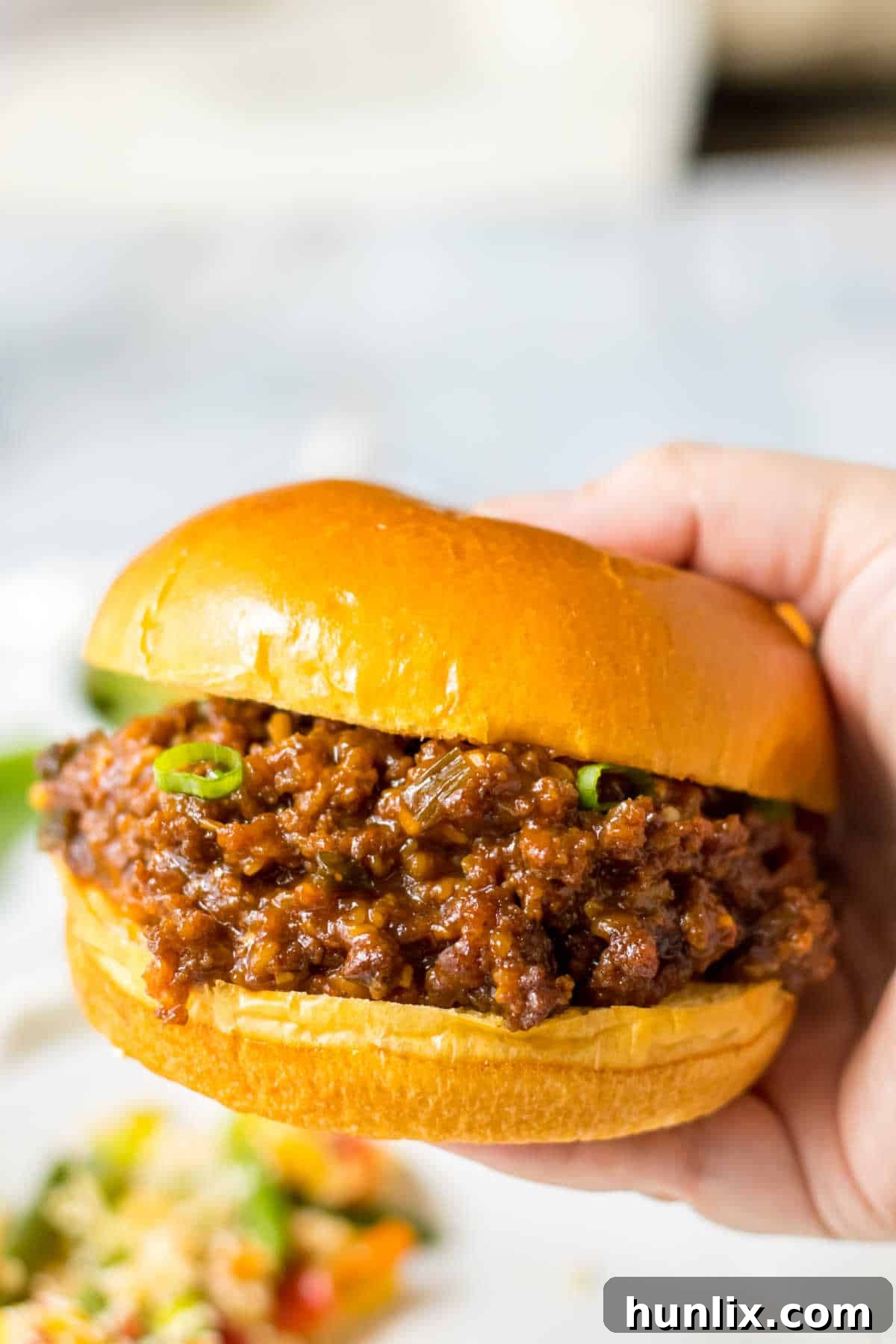 A hand holding a Korean sloppy joe sandwich, ready to be eaten.