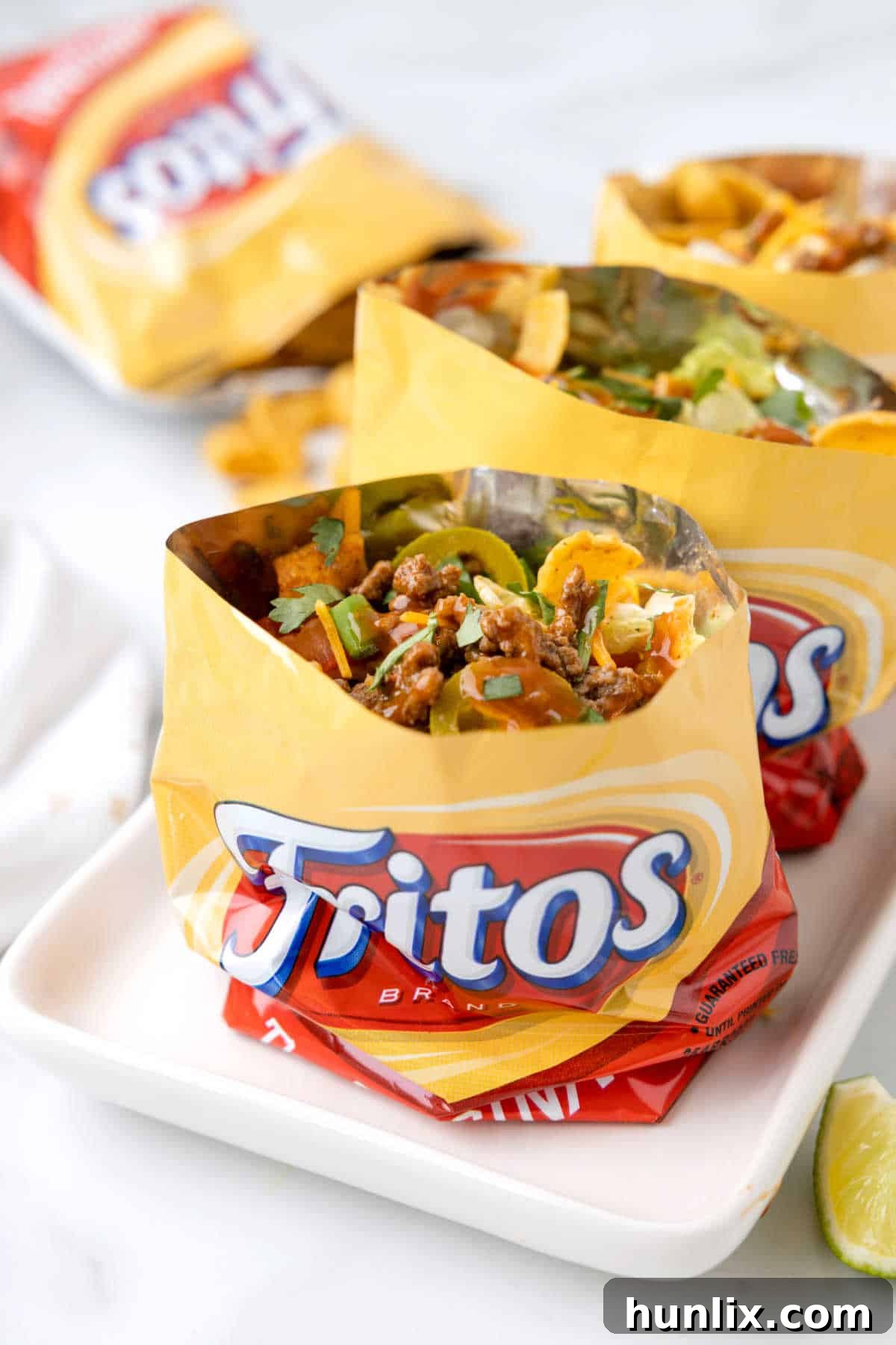 A vibrant platter showcasing several Walking Tacos in individual Frito bags, each overflowing with seasoned beef, shredded cheese, and fresh toppings.