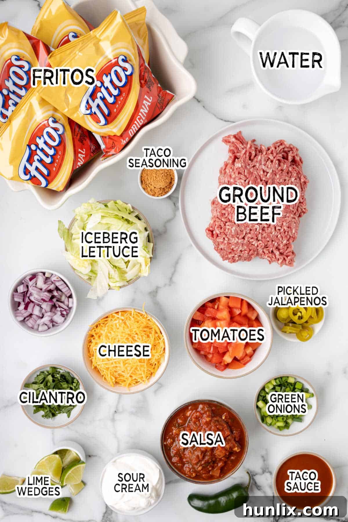 All the core ingredients for Walking Tacos neatly laid out on a white countertop, including ground beef, taco seasoning, water, and snack-size Frito bags.