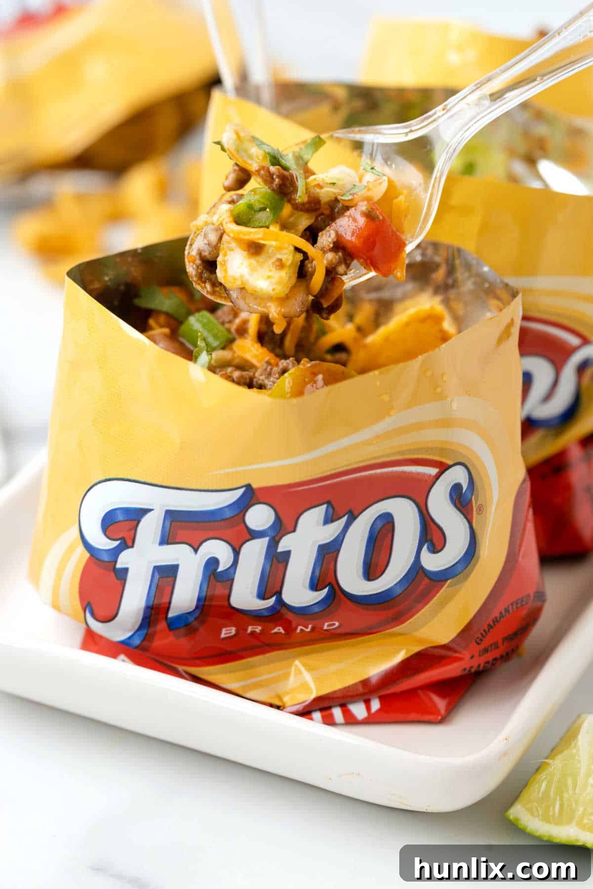 A close-up shot of a Walking Taco in a Frito bag, held with a spoon, showing the layers of seasoned beef and melted cheese.