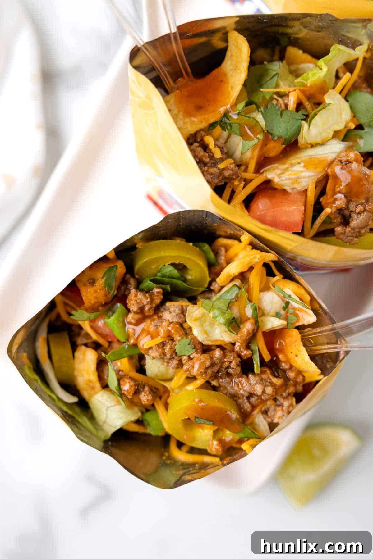 An overhead view of an assembled Walking Taco in a chip bag, with a spoon digging into the layers of meat and toppings, ready to be eaten.