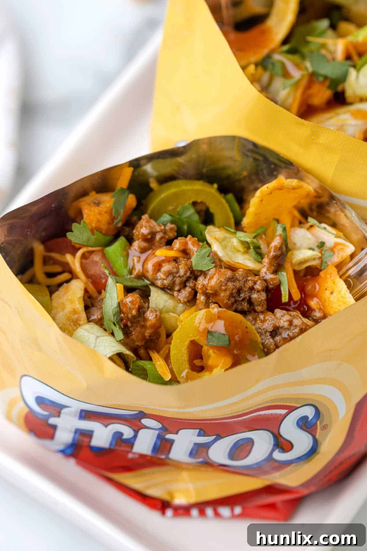 Several Walking Tacos arranged on a large platter, each featuring abundant toppings like cheese, lettuce, tomatoes, and sour cream, with a spoon in one of the bags.