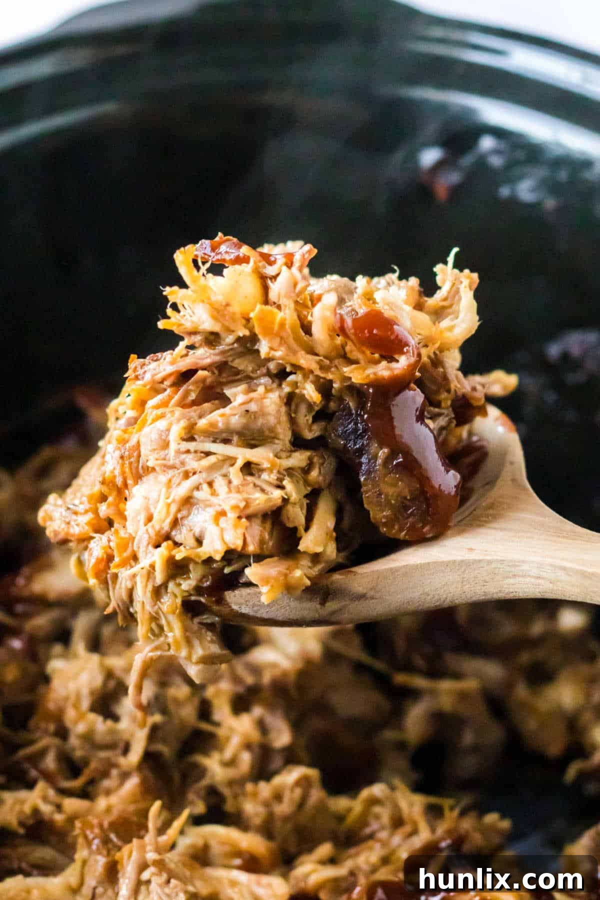 Root beer pulled pork served on a wooden serving spoon, highlighting its moist and tender texture.