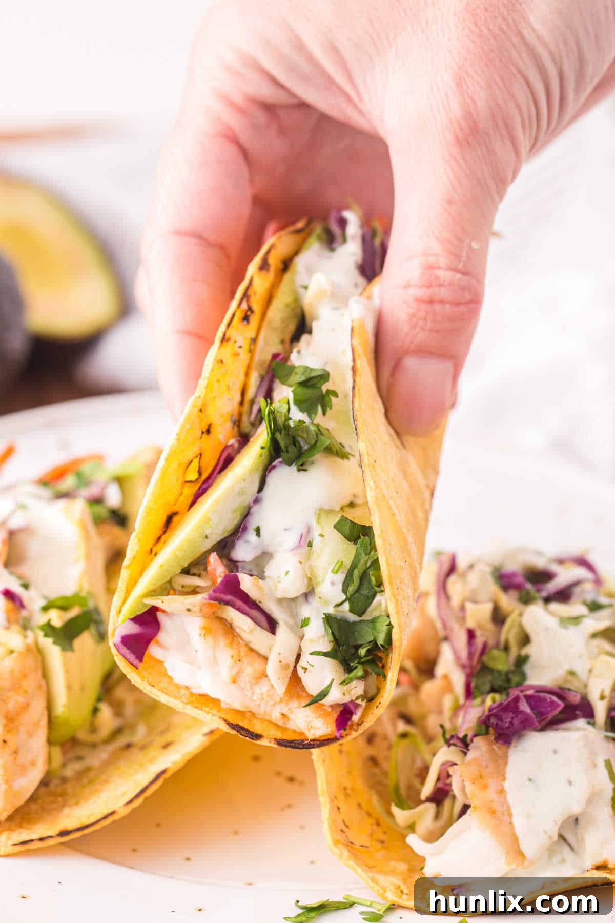 A hand holding a beautifully assembled fish taco with vibrant toppings.