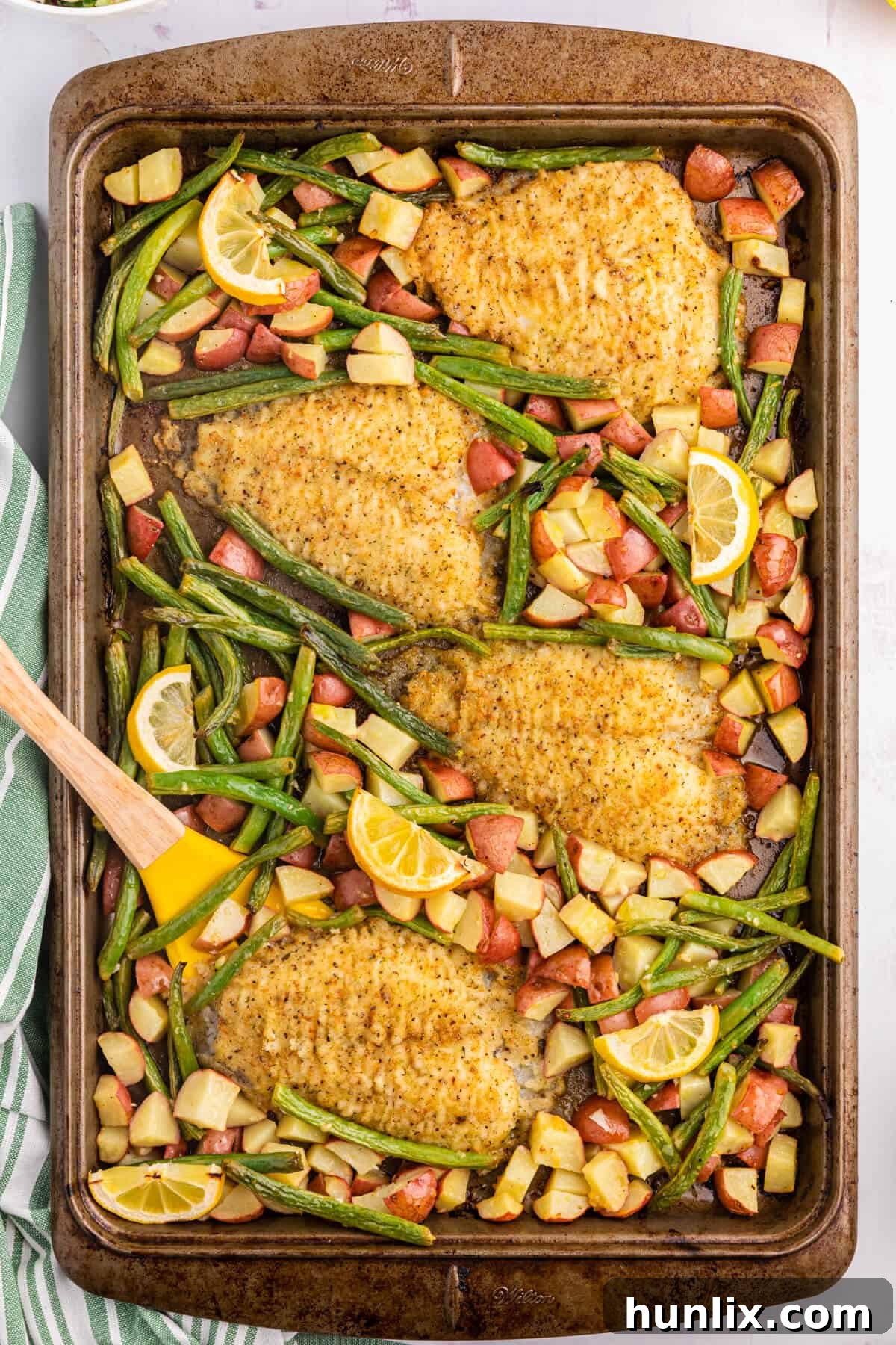 A serving spatula lifting a piece of perfectly cooked Lemon Pepper Sole from the sheet pan, alongside roasted potatoes and green beans, ready to be enjoyed.