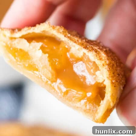 A hand holding a perfectly air-fried caramel apple empanada, cut in half to reveal its warm, gooey filling.
