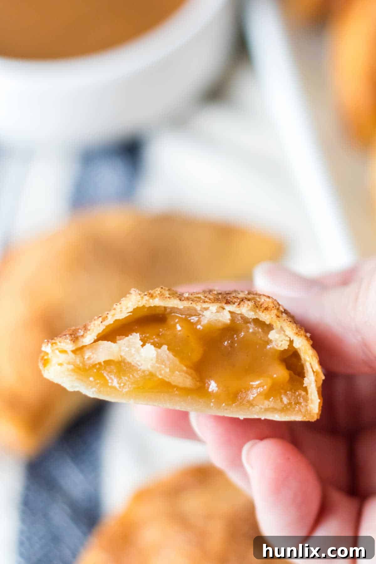 A hand holding a perfectly air-fried caramel apple empanada, cut in half to reveal its warm, gooey filling.