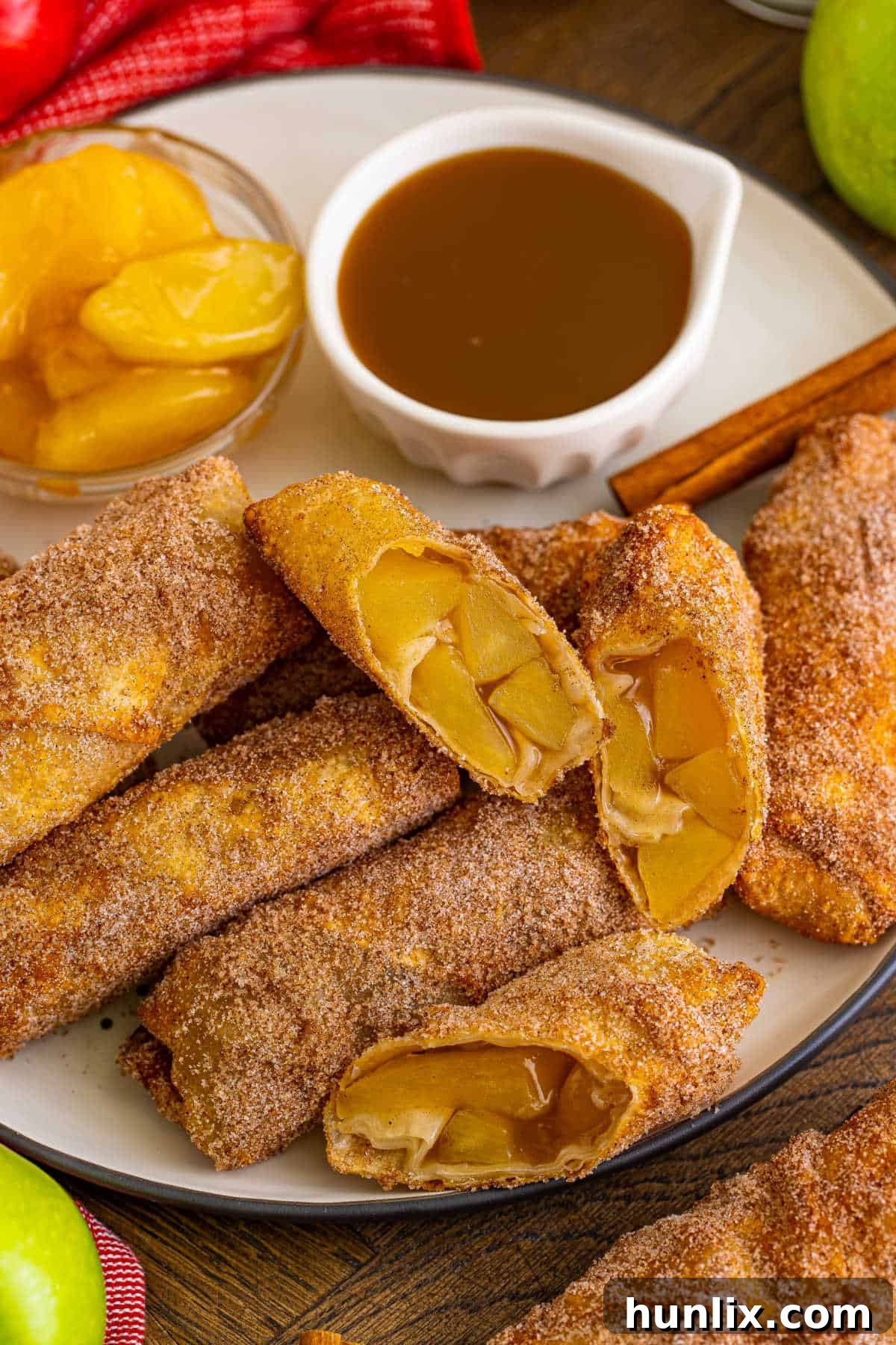 A plate of golden apple pie egg rolls with a small bowl of rich caramel dipping sauce beside them, ready to be enjoyed.