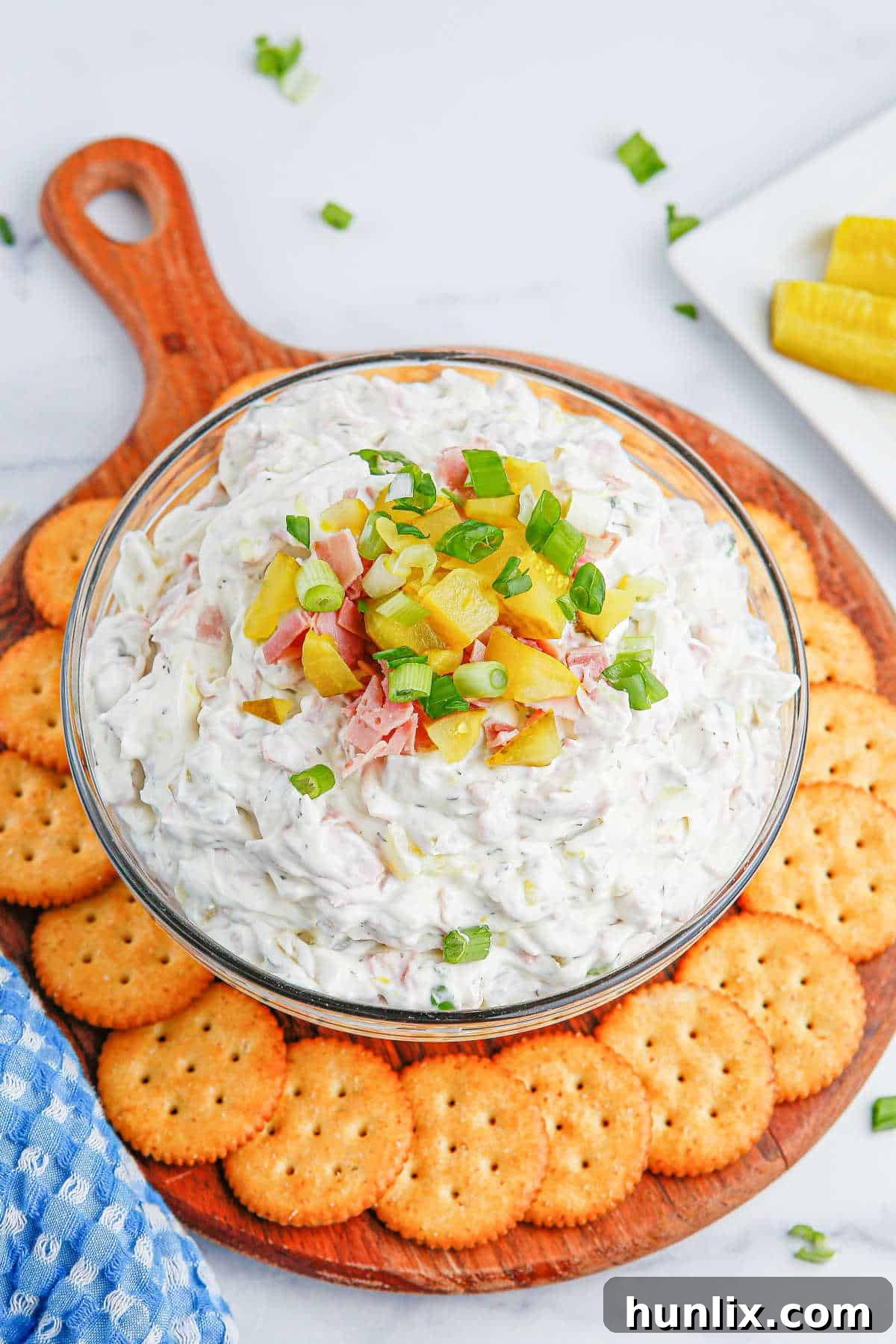 A bowl of creamy dill pickle dip surrounded by an array of crackers, ready for serving at a gathering.