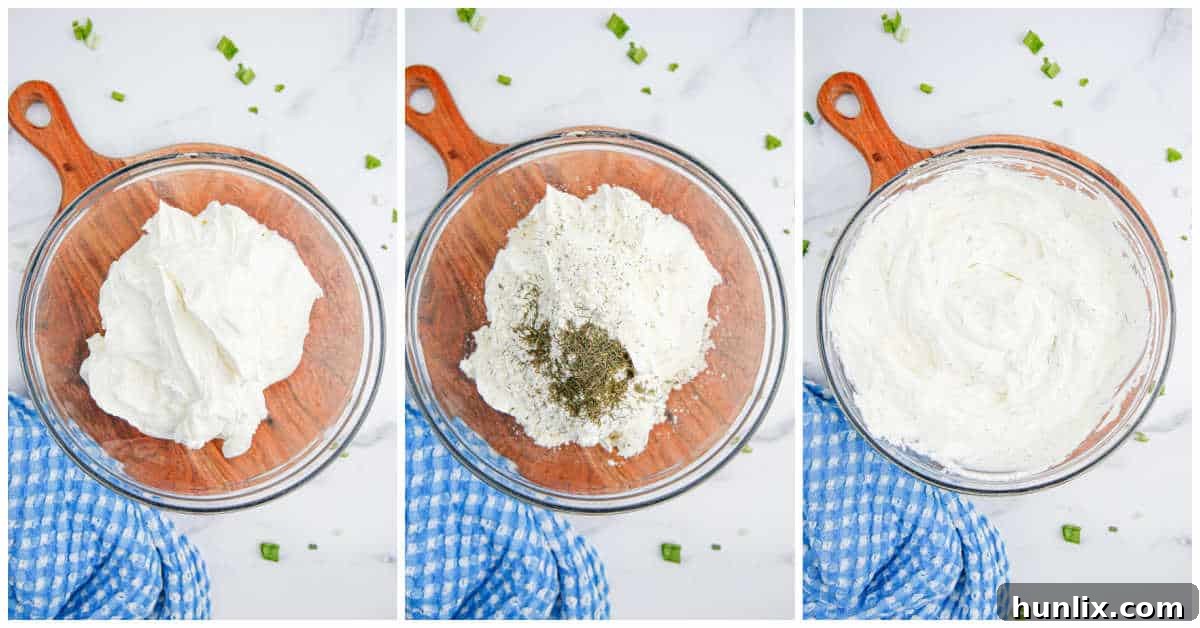 A close-up shot of a large mixing bowl where cream cheese, sour cream, ranch seasoning, and dried dill are being blended together with a spatula, creating the smooth, creamy base of the dill pickle dip.