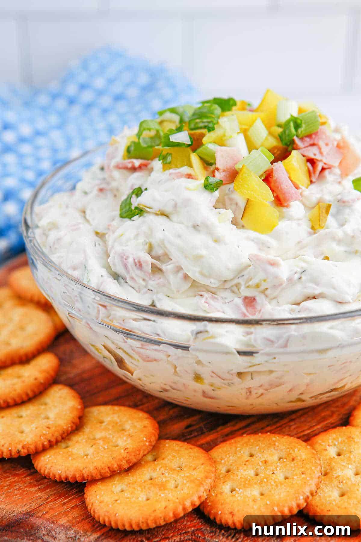 A serving bowl of dill pickle dip placed on a rustic wooden board, surrounded by a selection of crackers and fresh herbs, emphasizing its inviting and delicious appearance.